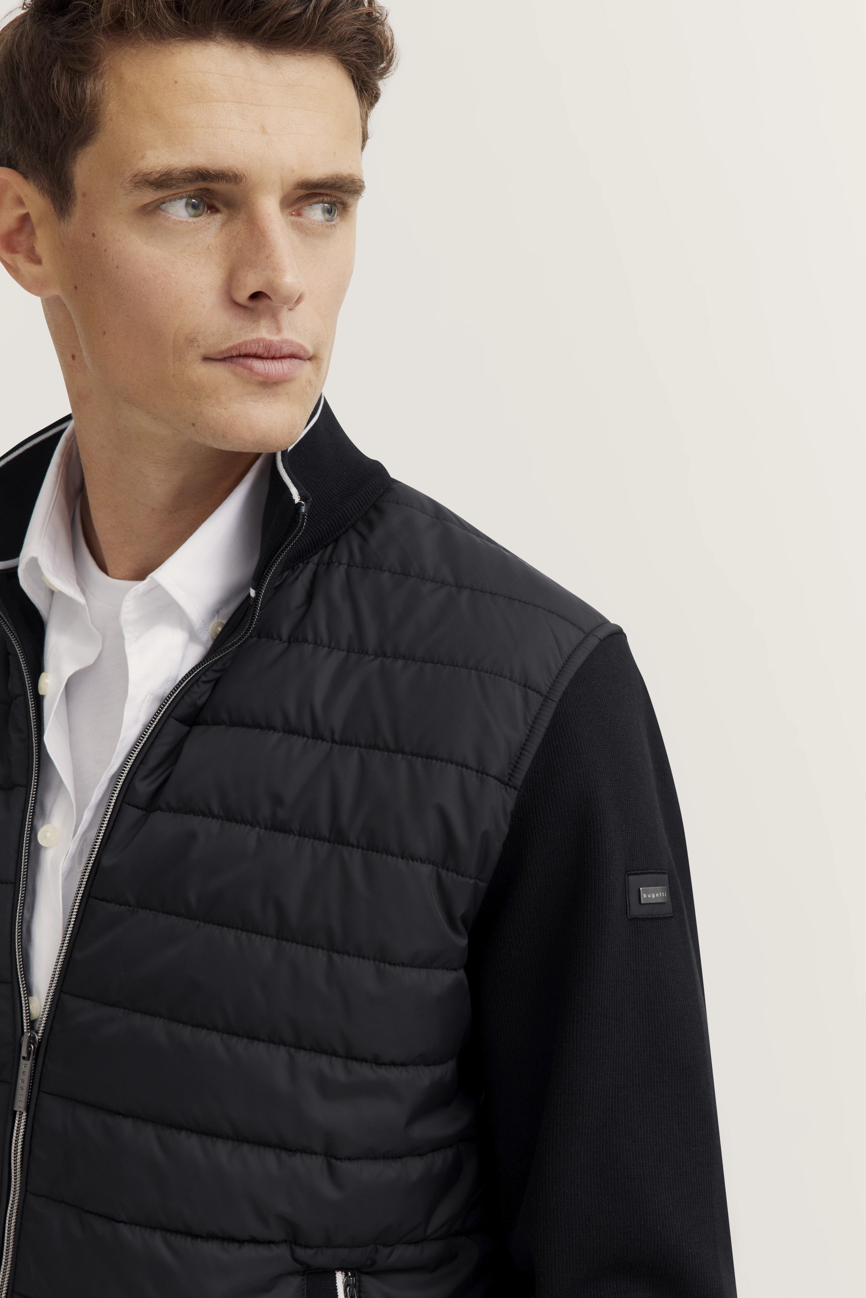 Model trägt bugatti schwarze Steppjacke über weißem Hemd, legerer Look, Blick nach links.