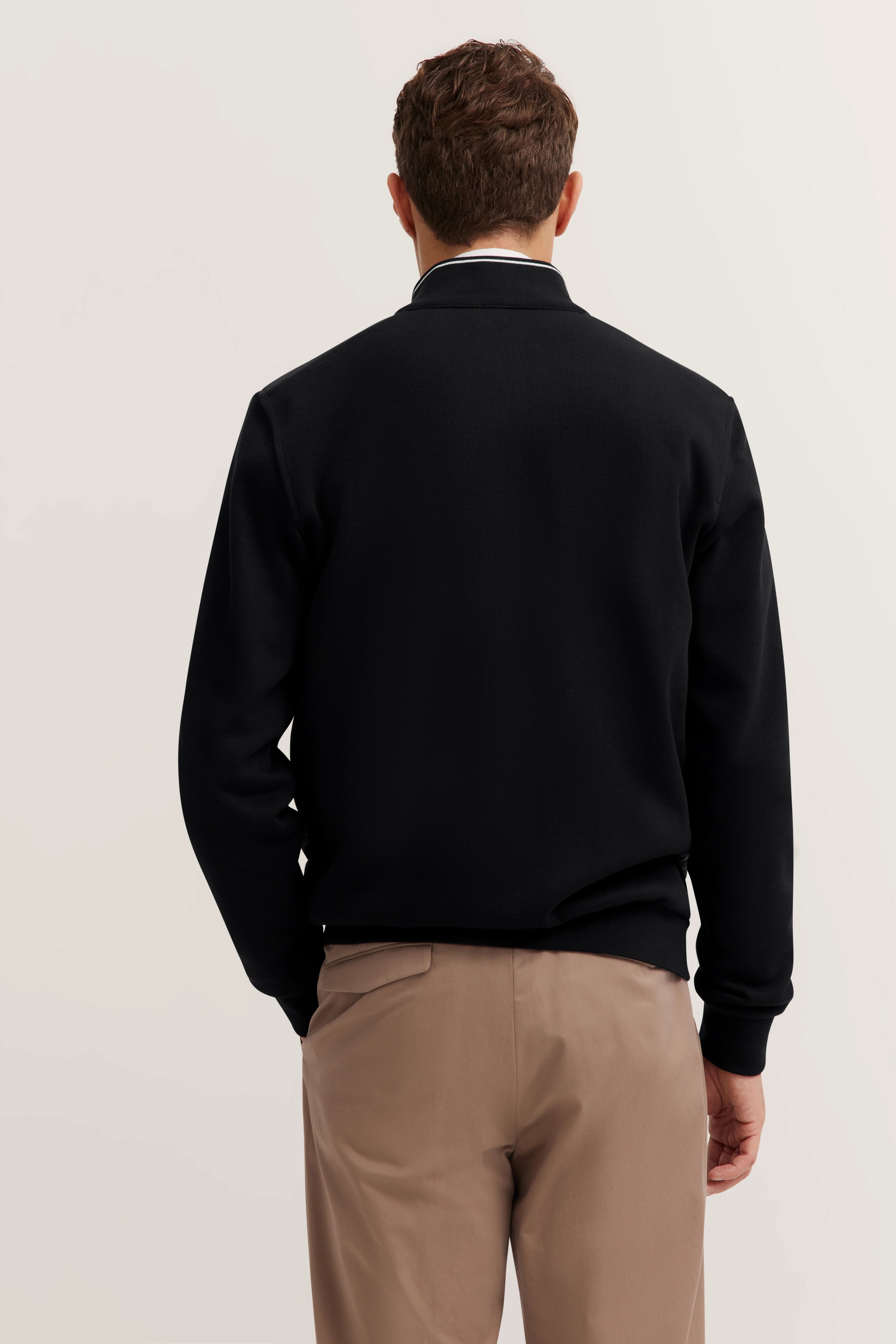 Schwarzer Pullover und beige Hose, Rückansicht auf Model, schlichtes Design.