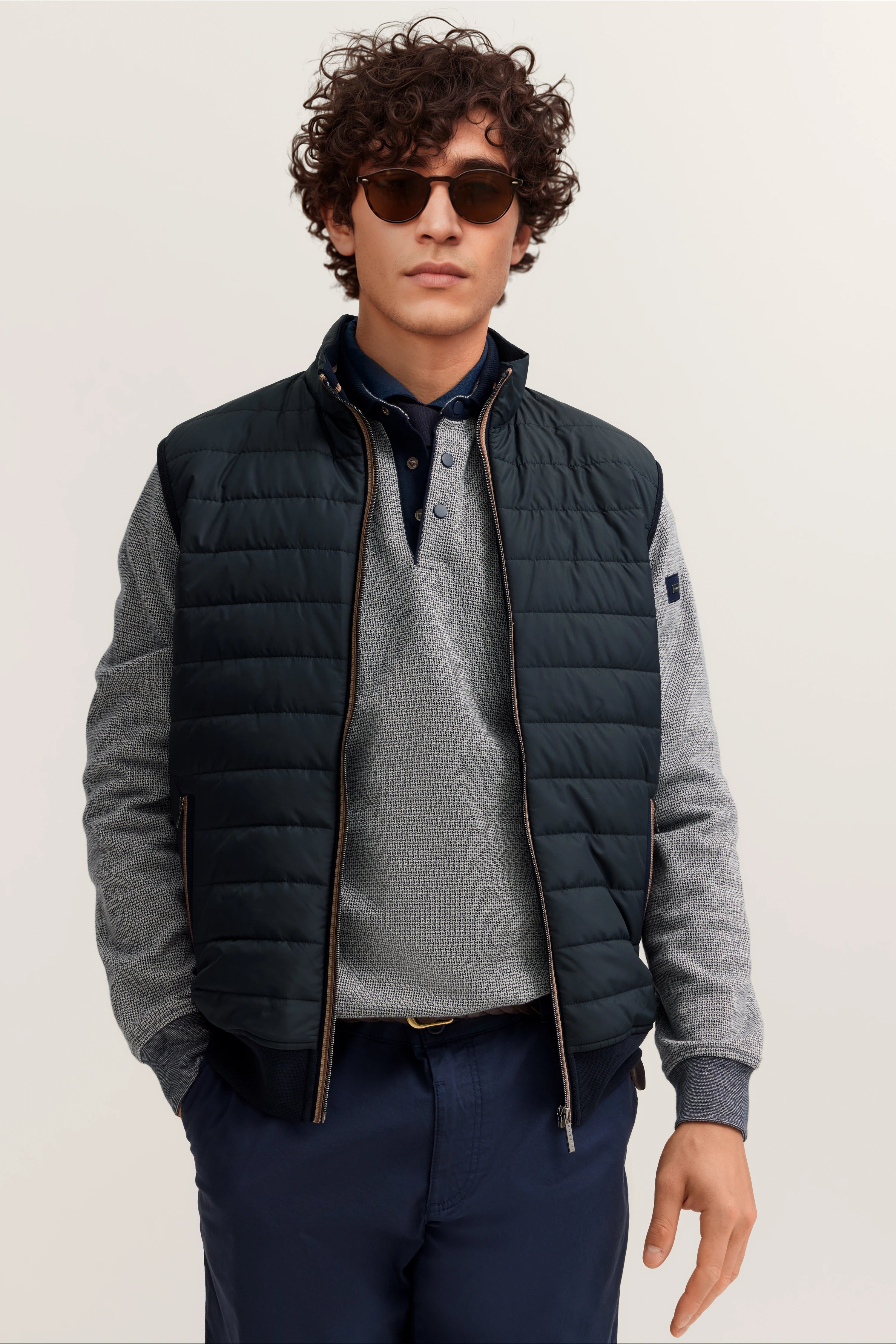 Model in blauer Steppweste, grauem Pullover und blauer Chinohose von bugatti, entspanntes Posing.