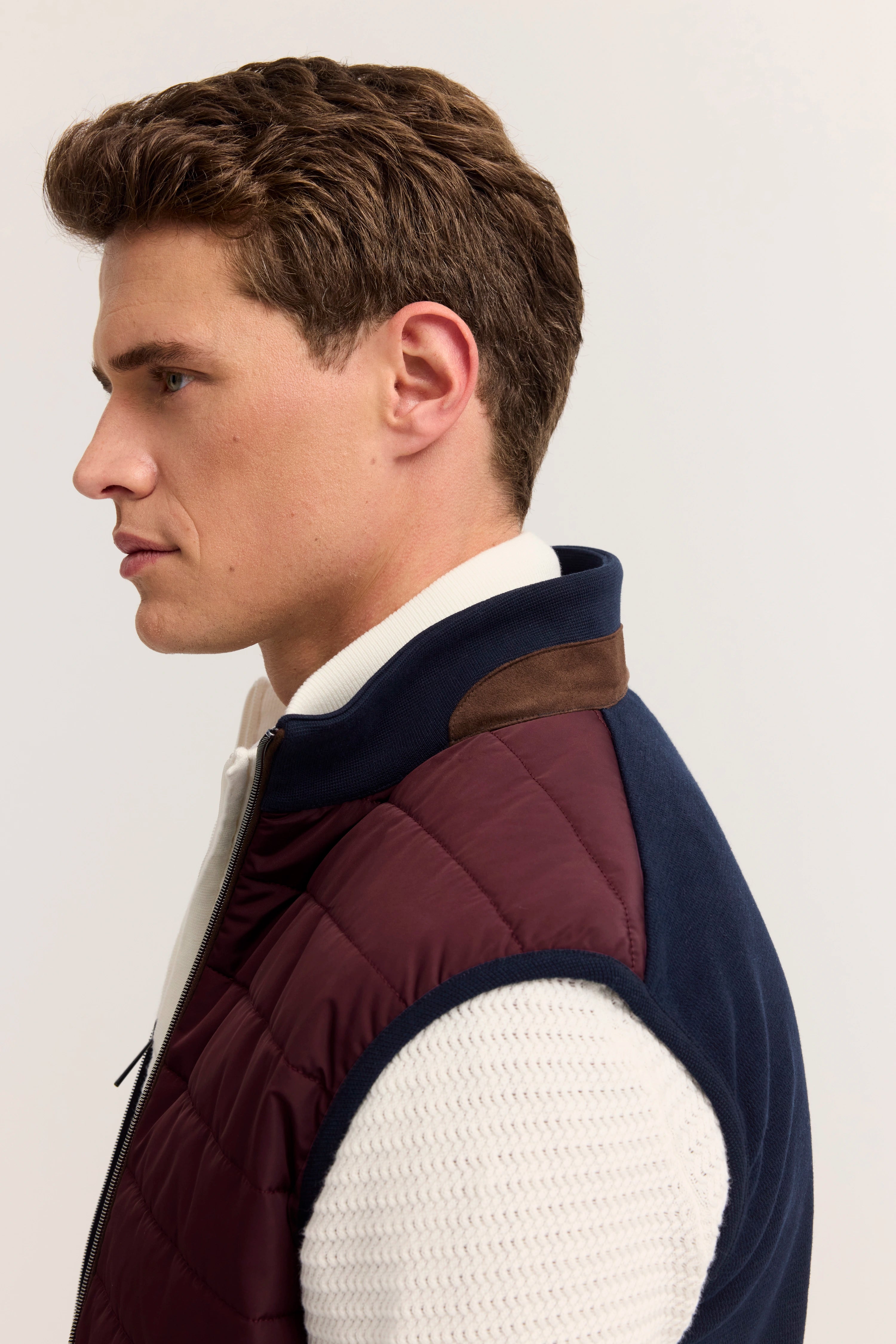 Büstenbild von bugatti: marineblaue und burgunderrote Steppweste über cremefarbenem Strickpullover.