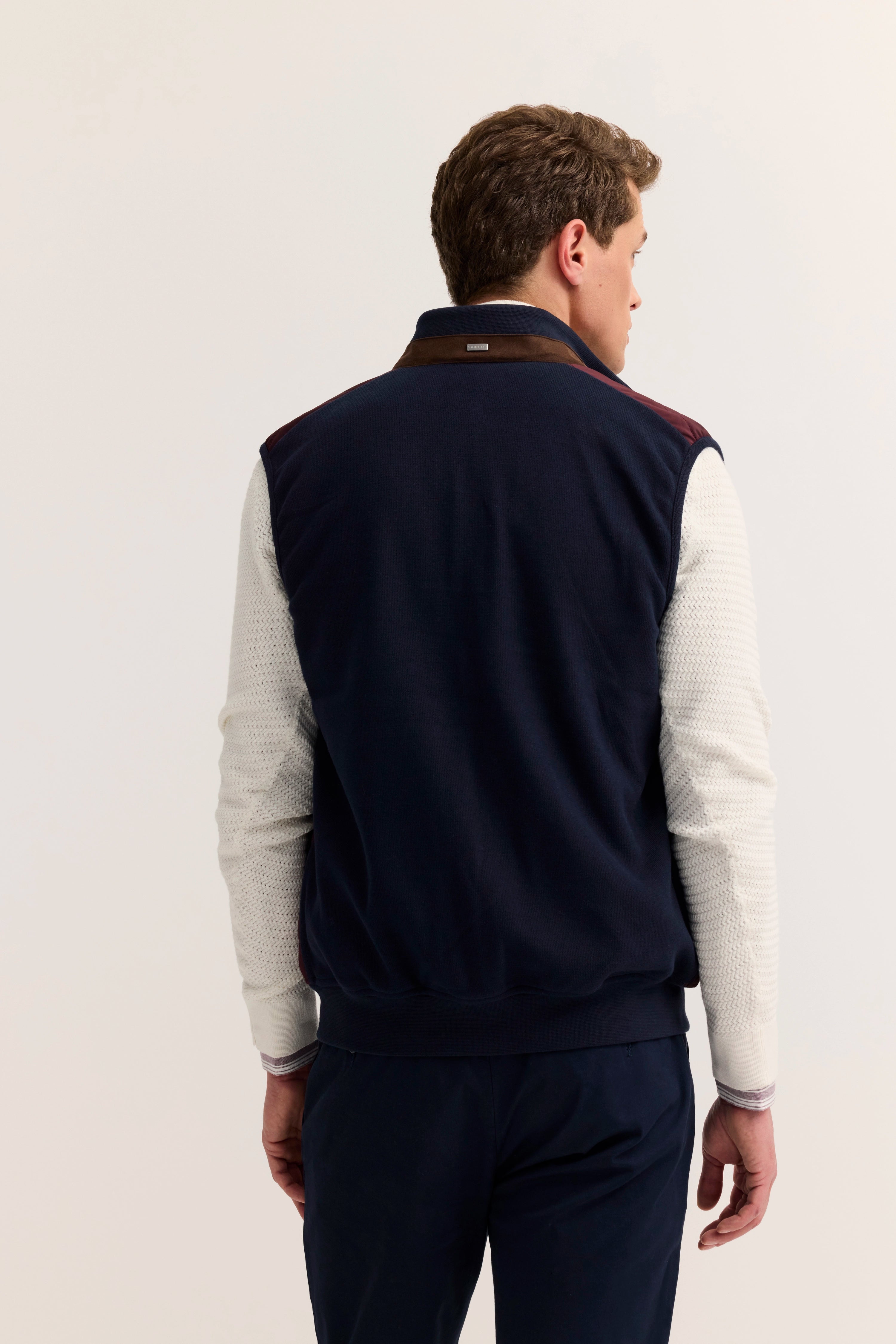 Rückansicht Model in navy Weste, creme Pullover, marine Hose, legeres Posing, bugatti Stil.