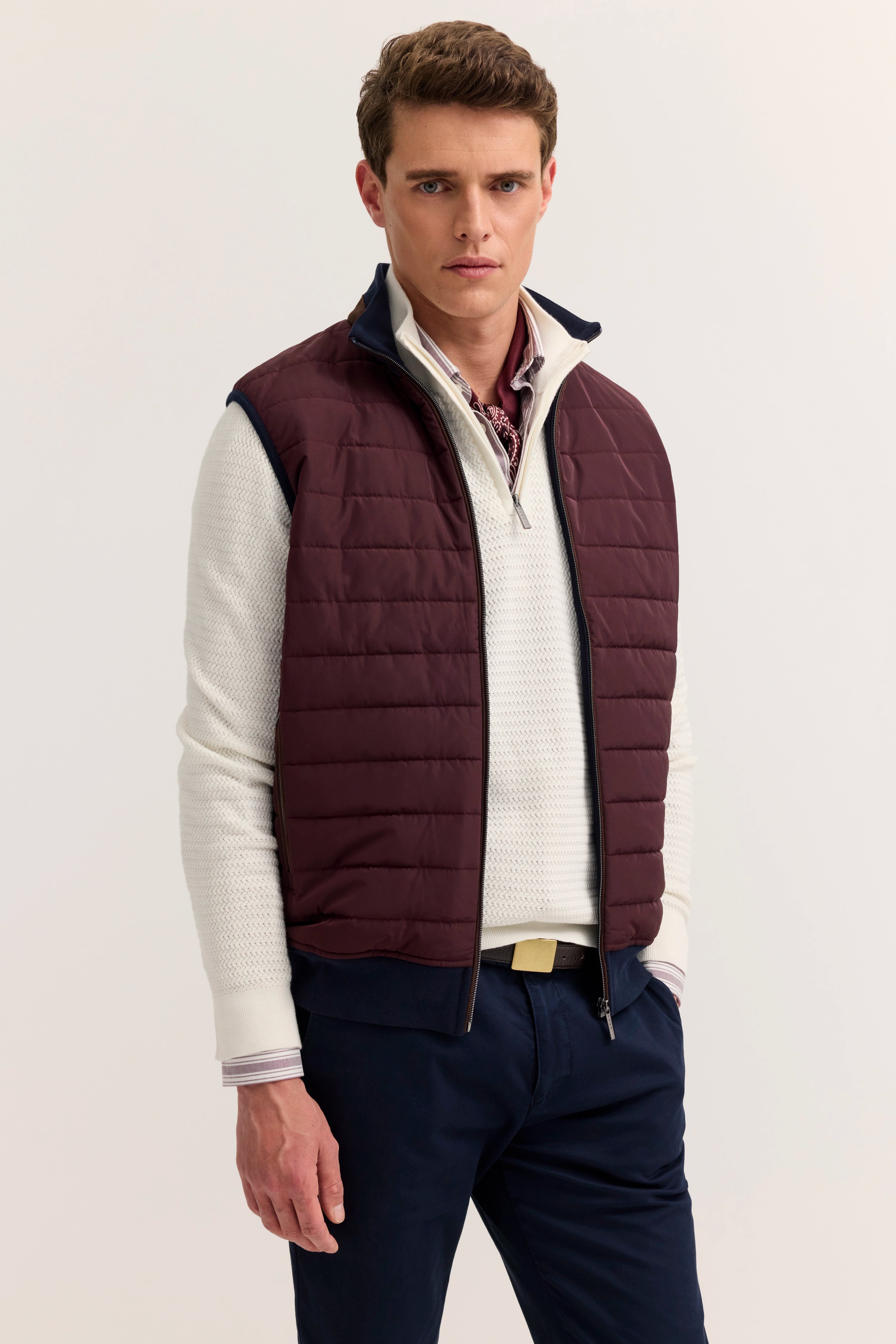 "bugatti Modelbild: Burgunder Steppweste, cremefarbener Pullover, marineblaue Hose, legeres Posing"