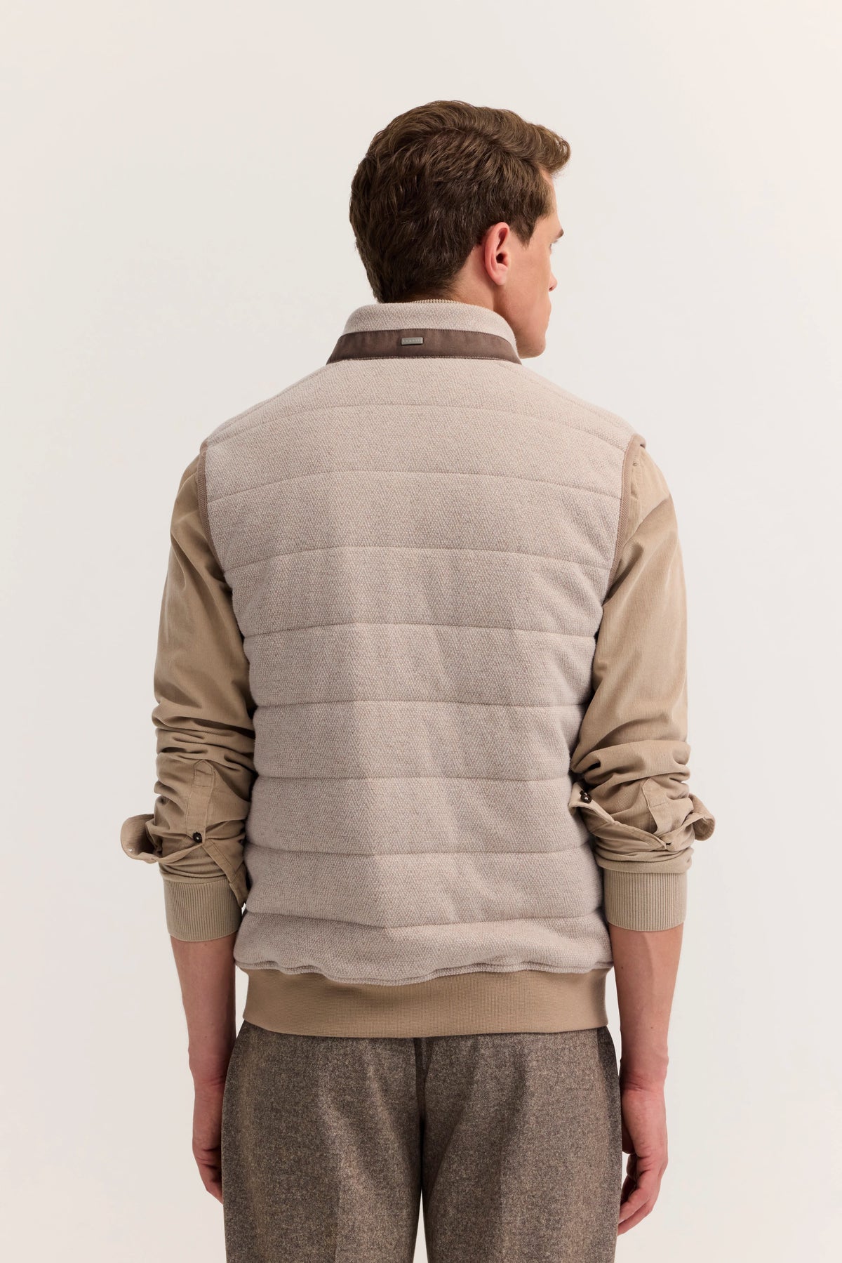 Rückansicht Model in beige Steppweste und Hemd, lässige Pose.
