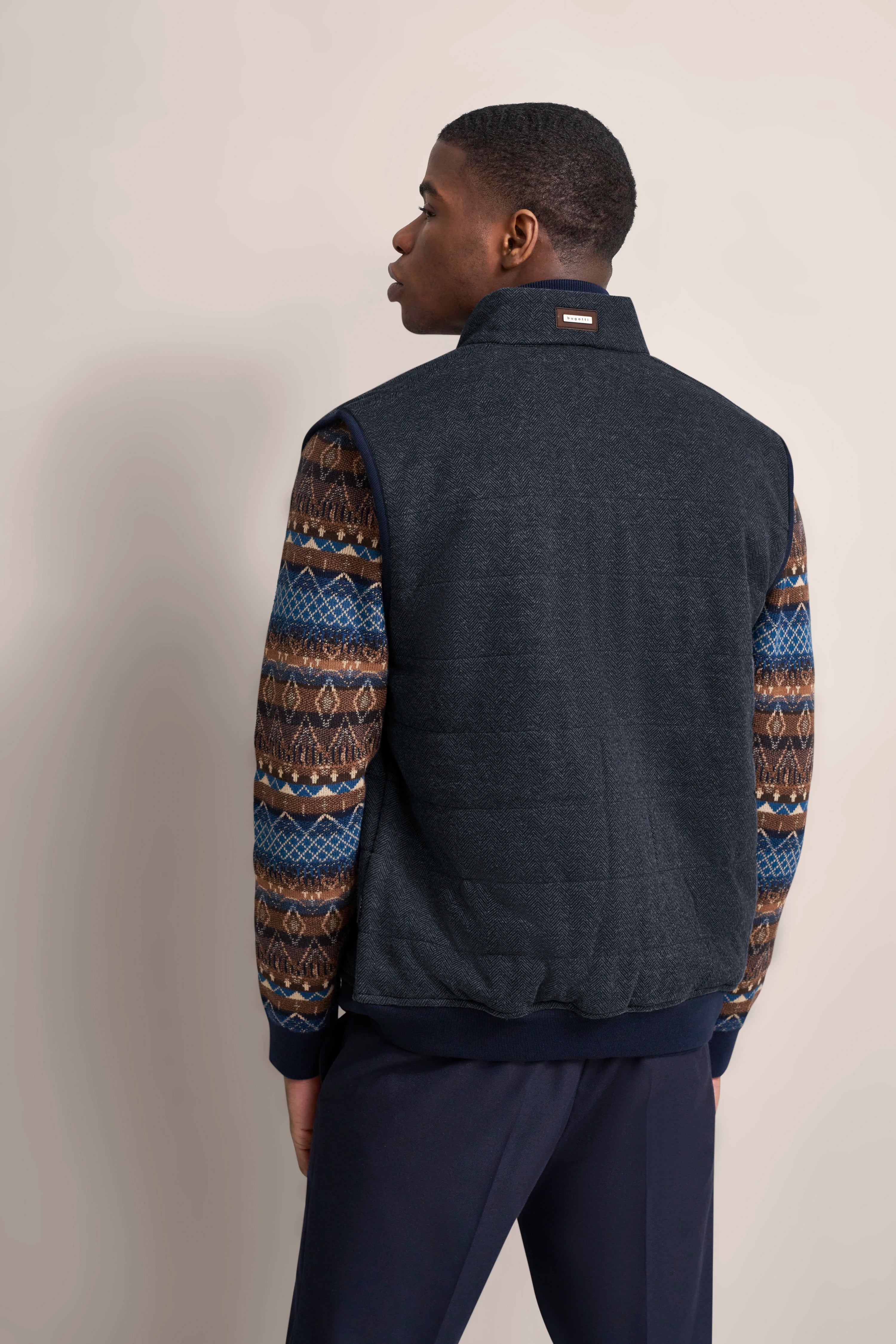 bugatti Modelbild, Rückansicht: Dunkelblaue Weste über gemustertem Pullover in Braun-Blau, lässig posiert.