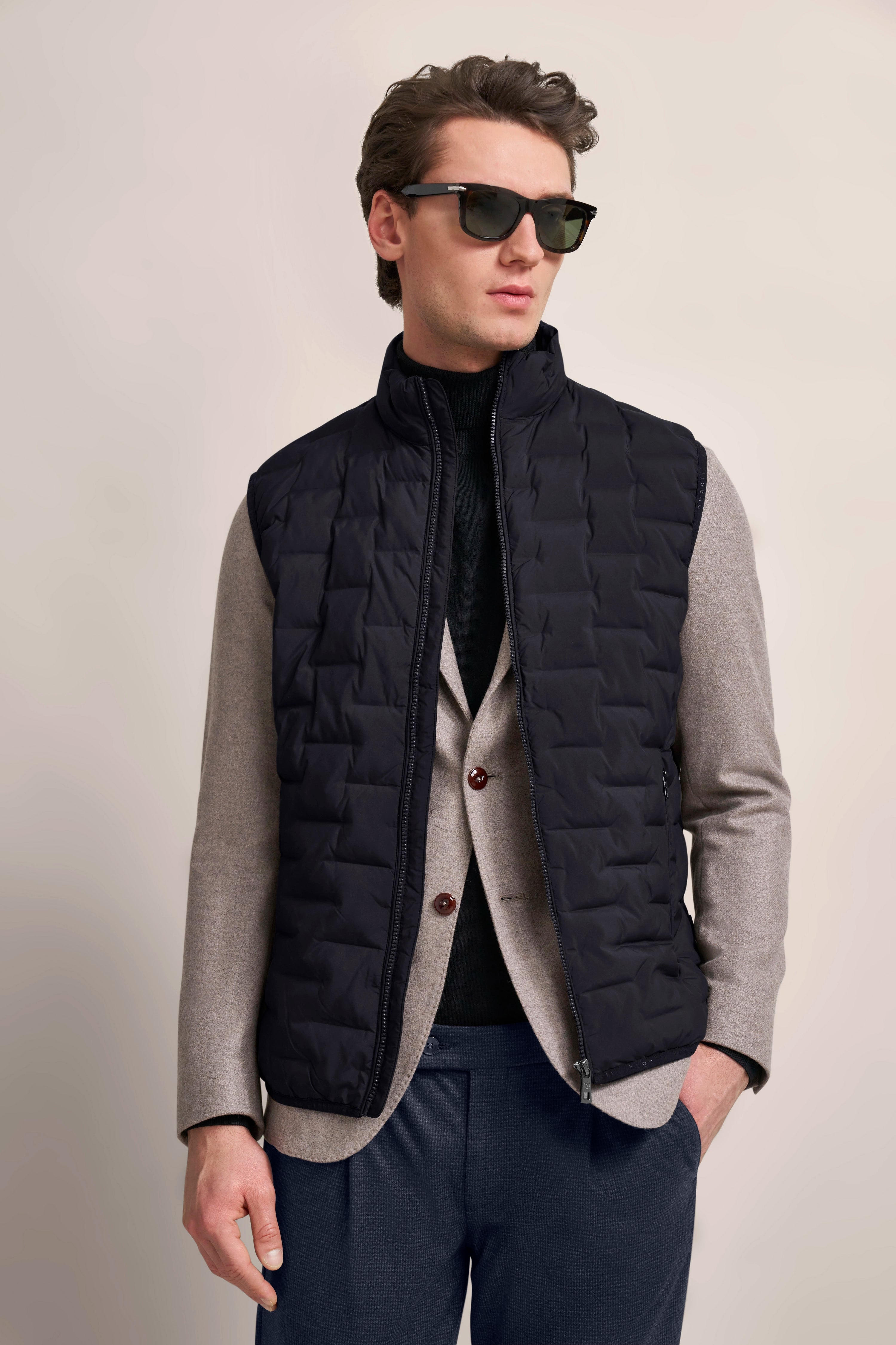 bugatti Outfit: schwarzes Steppweste, grauer Blazer, schwarzer Pullover, blaue Hose