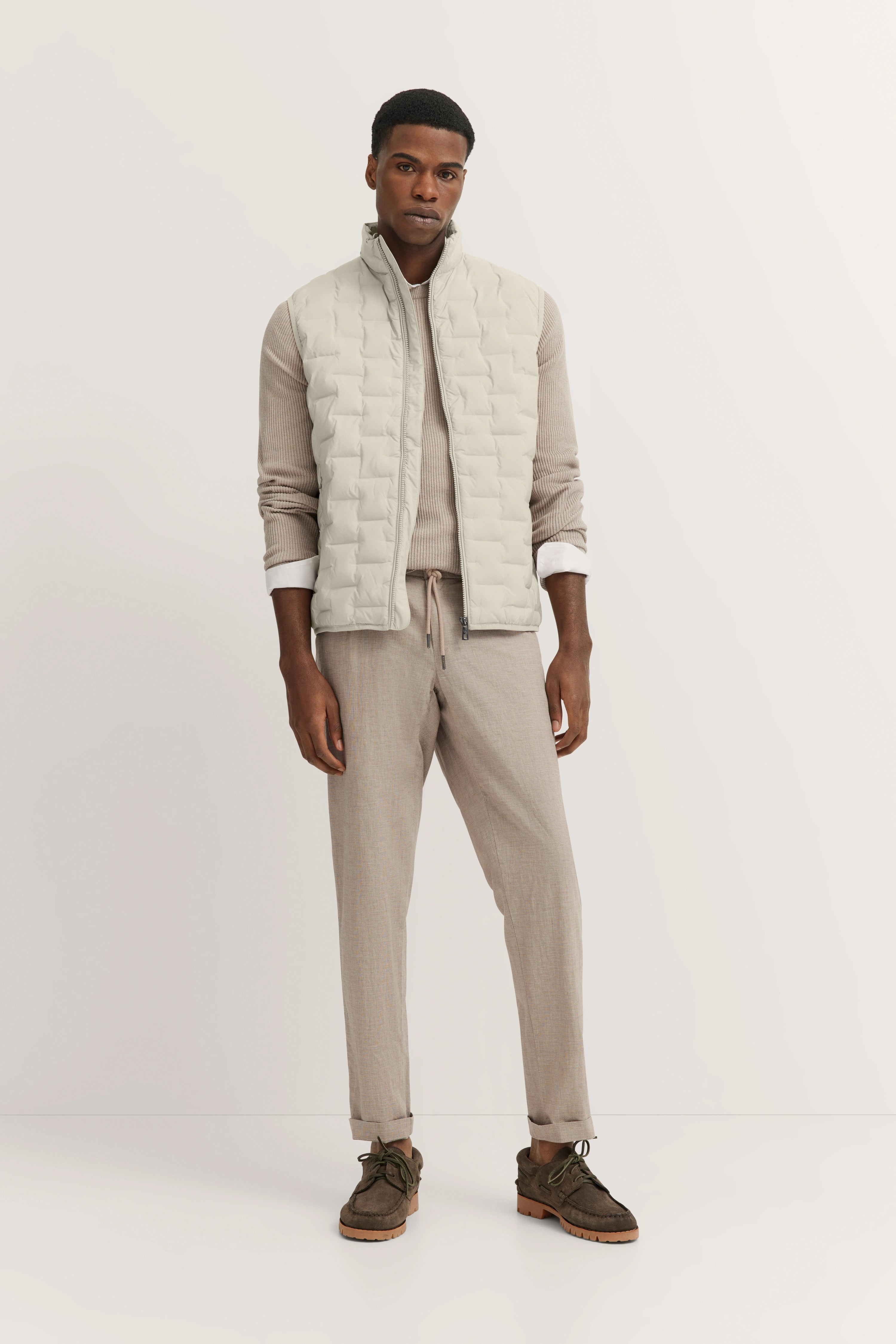 bugatti Modelbild: Beige Weste und Pullover, beige Hose, braune Schuhe, entspanntes Posing.