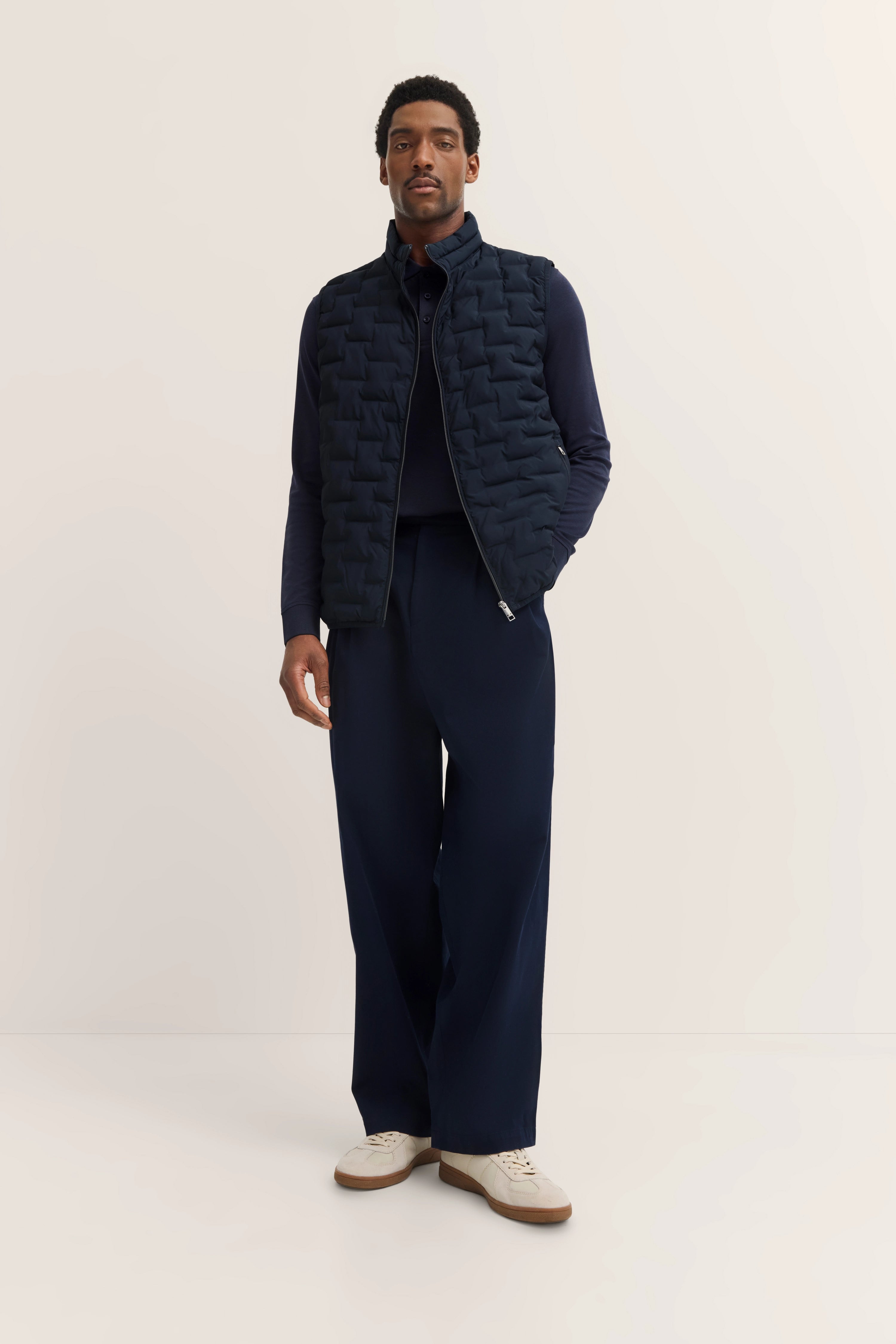 Model in navy bugatti Outfit mit Steppweste, Pullover und Hose, lässige Pose.