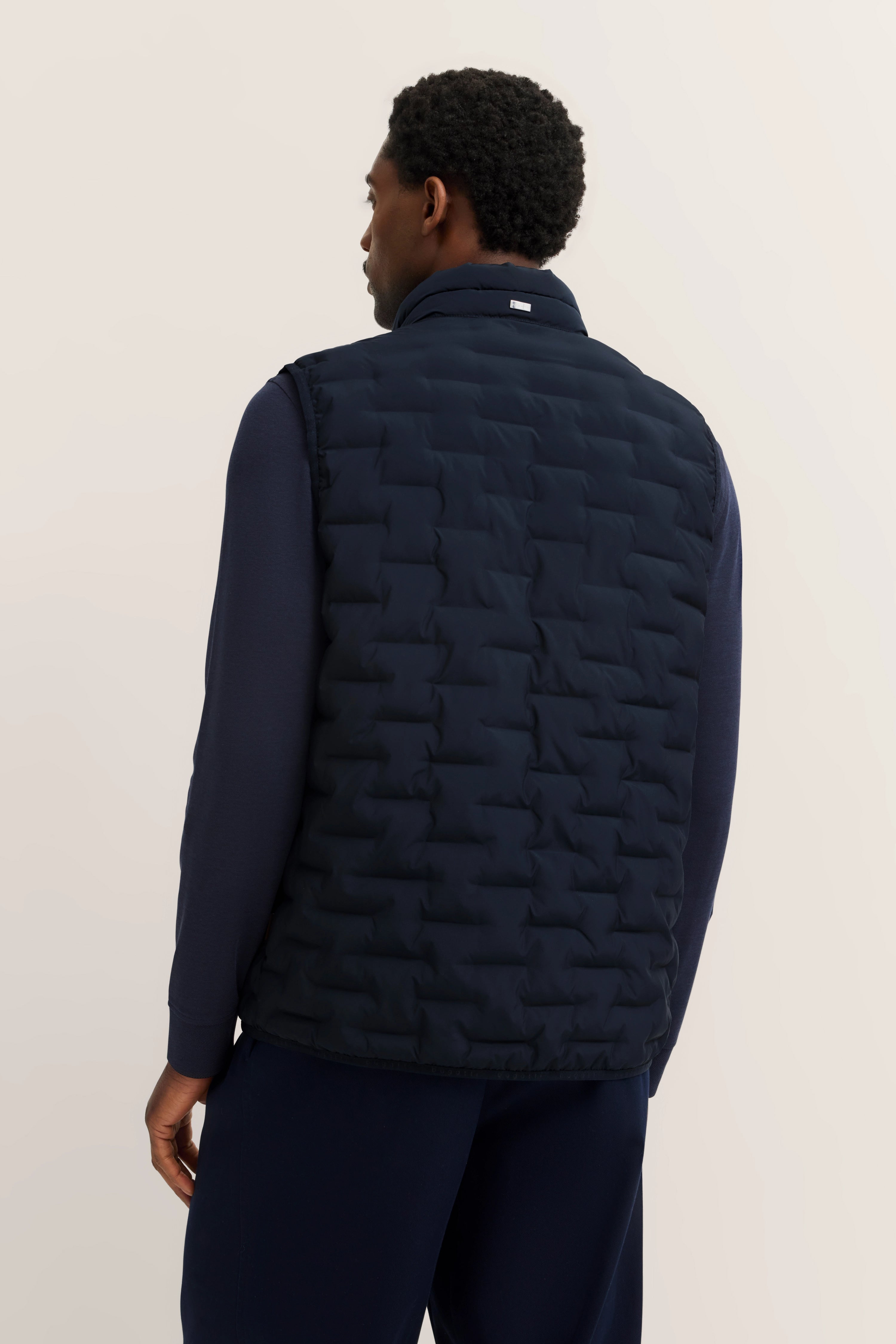 Schwarze Steppweste über dunkelblauem Langarmshirt, Rückansicht, legeres Modelbild.