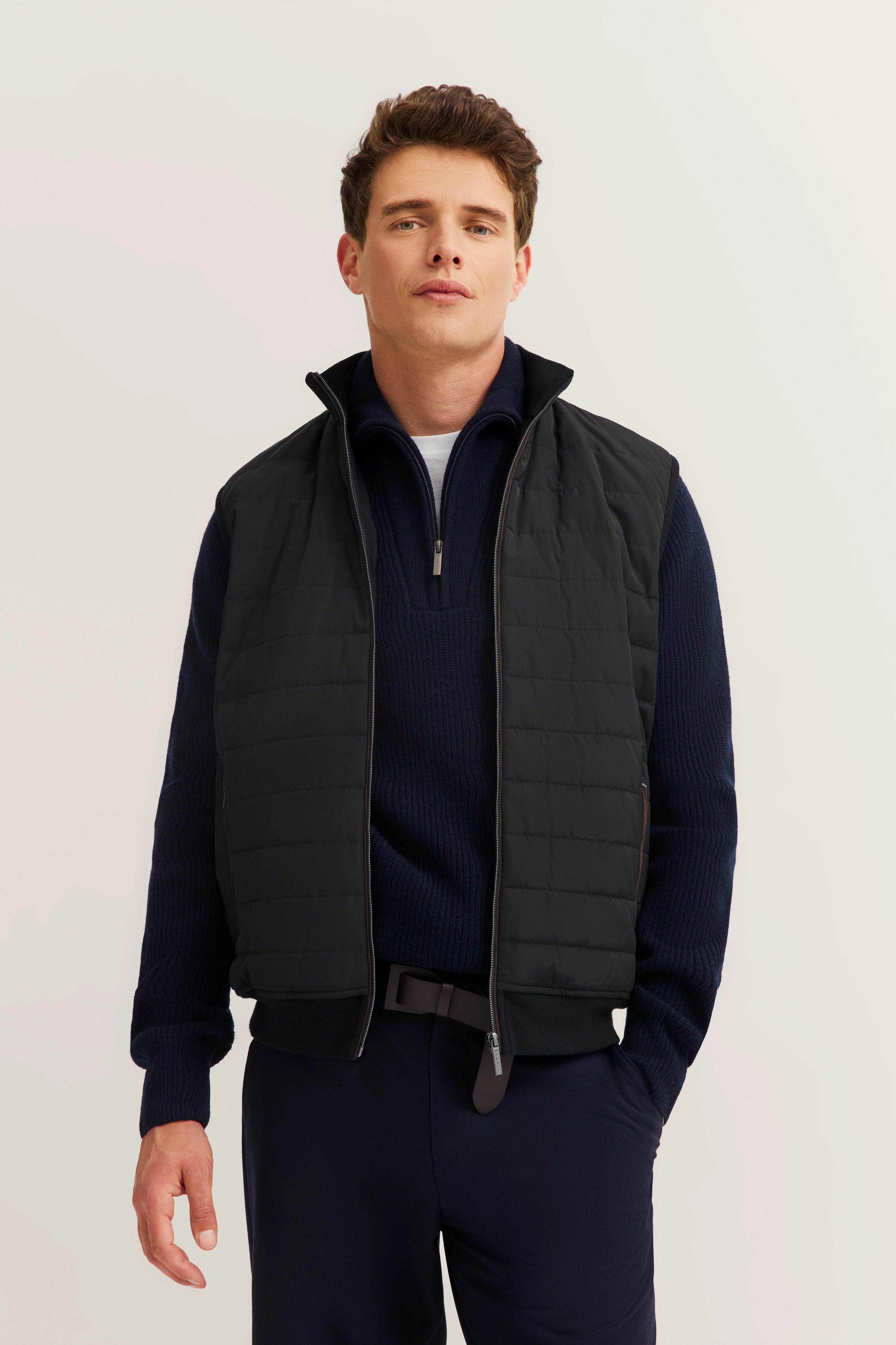 Schwarze Weste über dunkelblauem Pullover, Modelbild, entspanntes Posing, bugatti Stil.