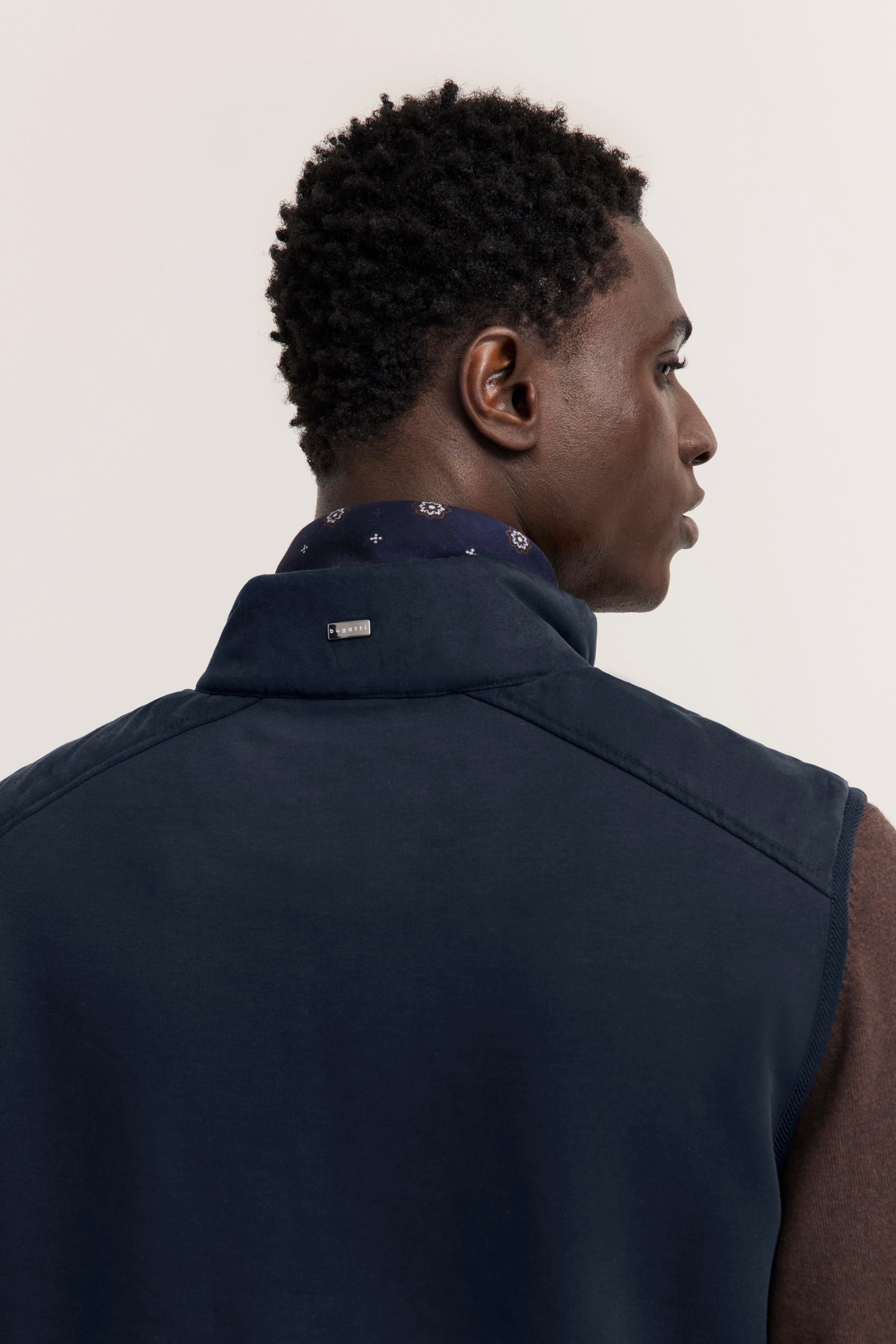 Rückansicht eines Models in marineblauer Weste mit braunem Langarmshirt und beigen Hosen von bugatti.