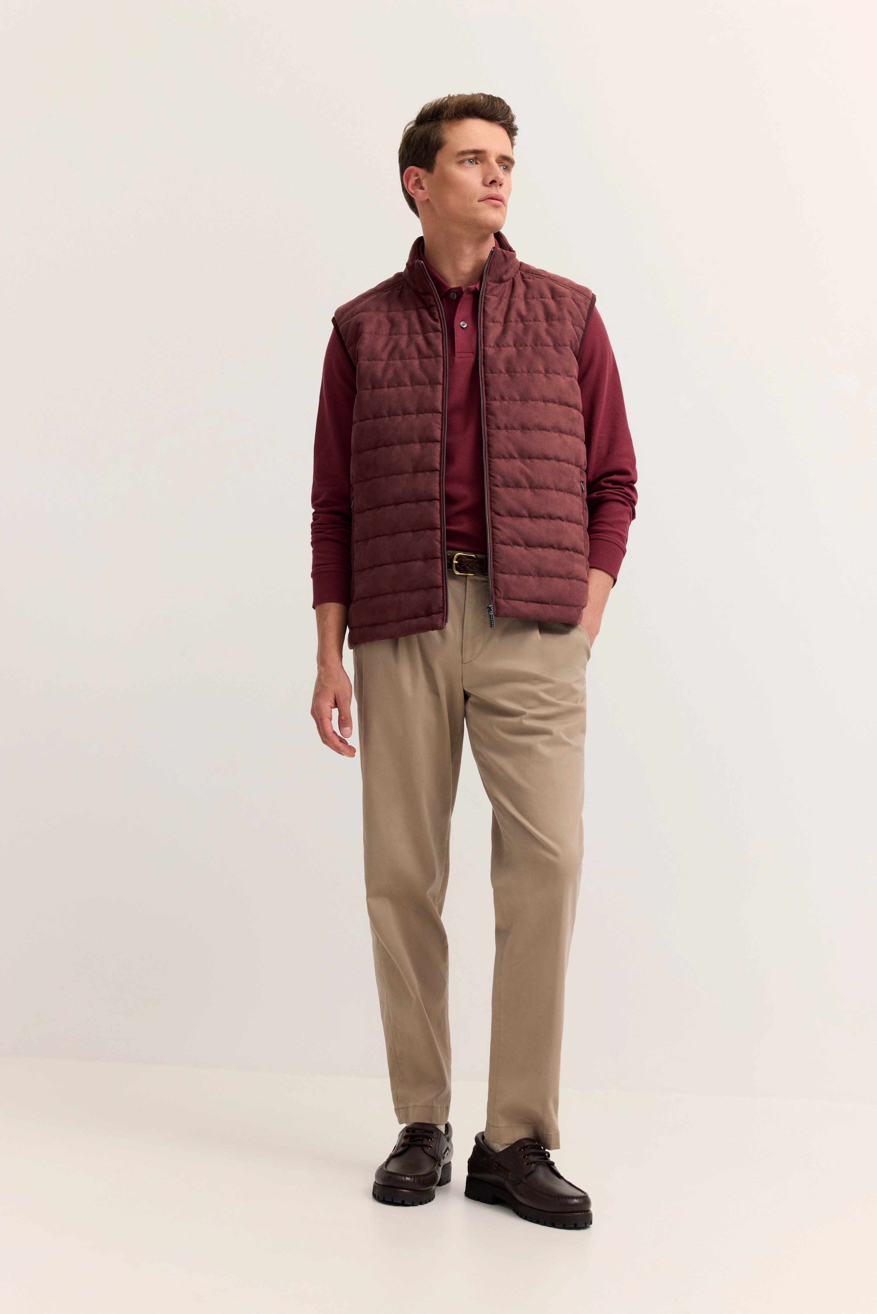 Bugatti Model in bordeaux Weste und Polo, beige Hose, braune Schuhe, entspanntes Posing.