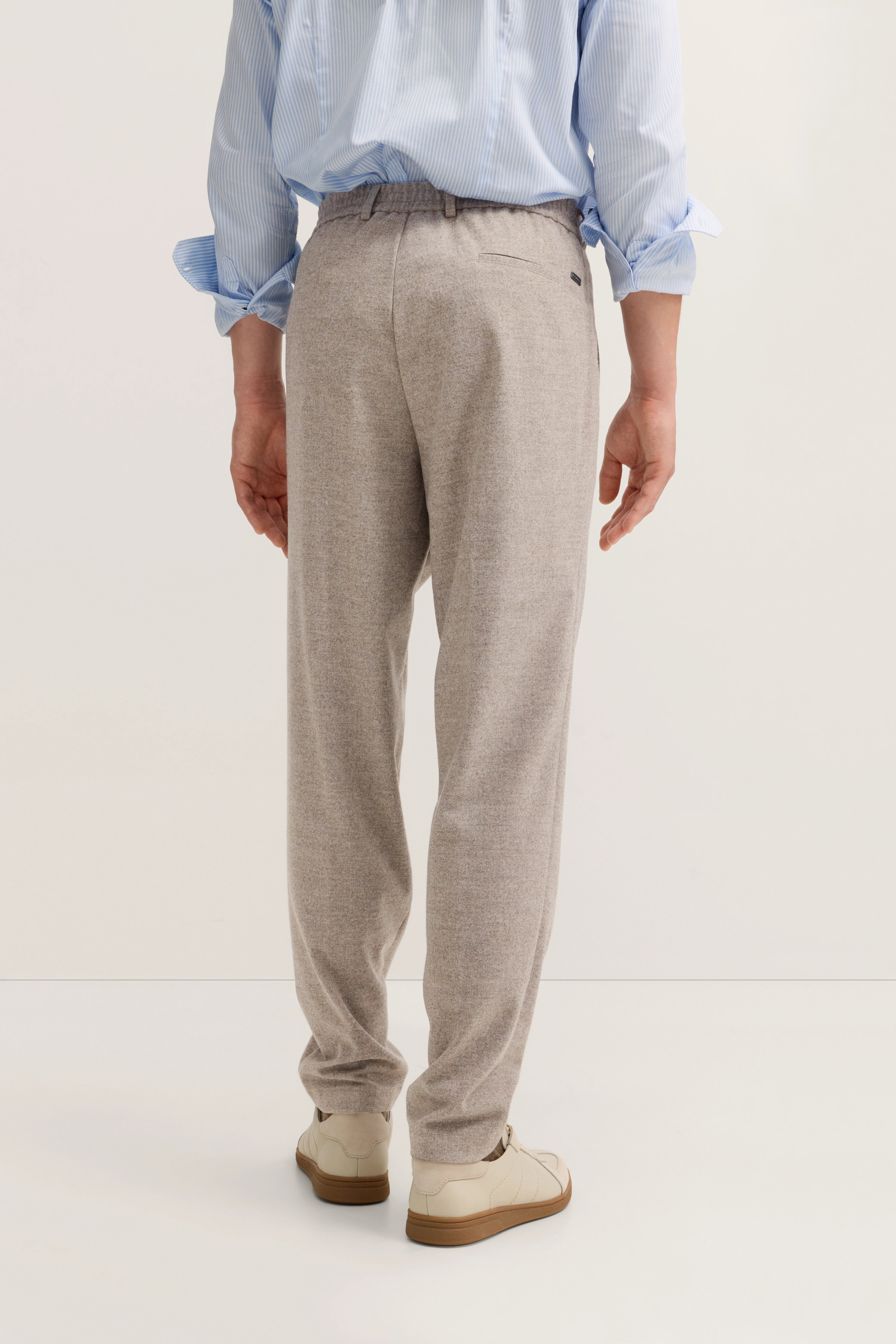 Beige Hose und hellblaues Hemd, legeres Modelbild, entspanntes Posing von hinten.