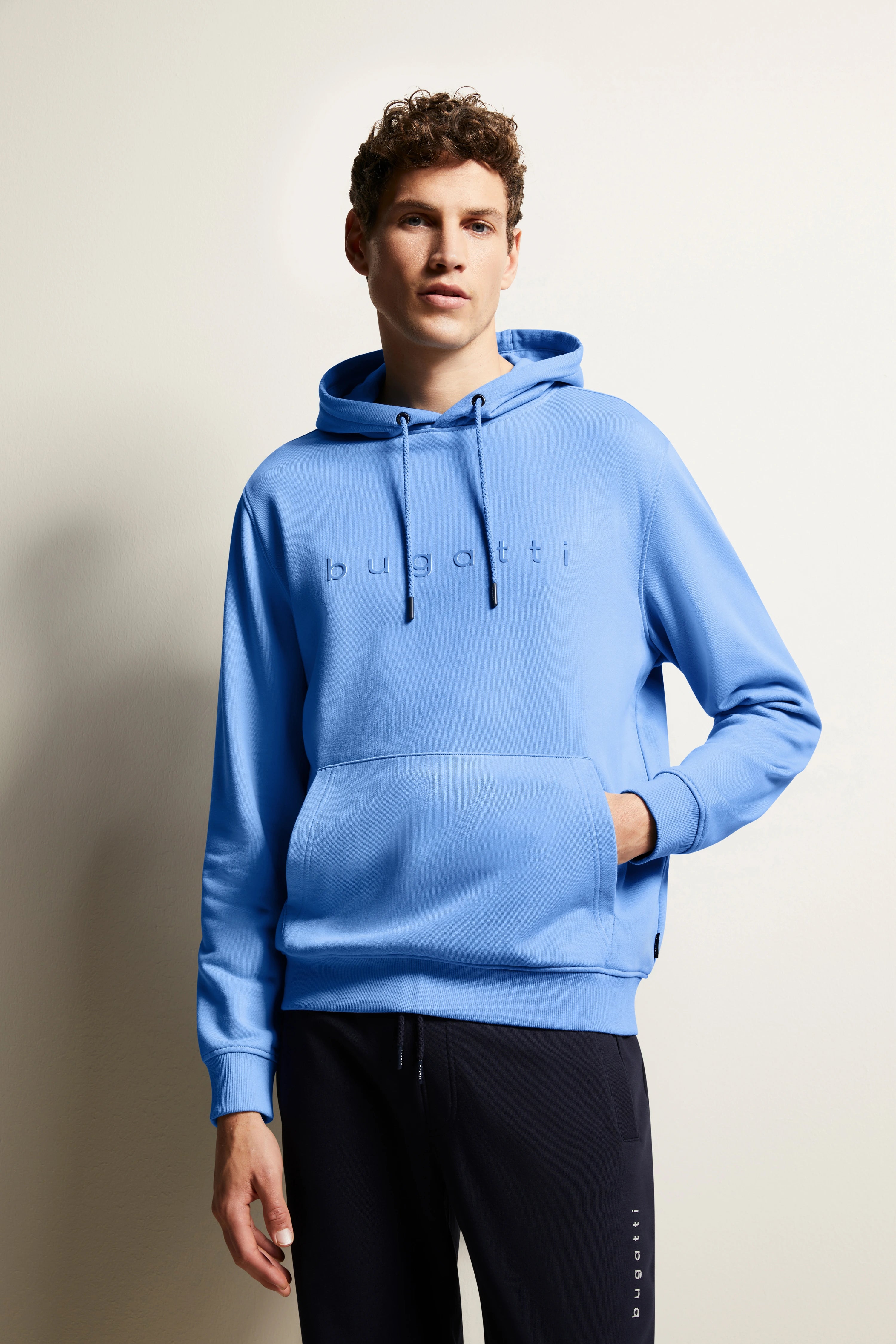 Model trägt blauen bugatti Hoodie mit schwarzer Jogginghose, entspannte Pose.