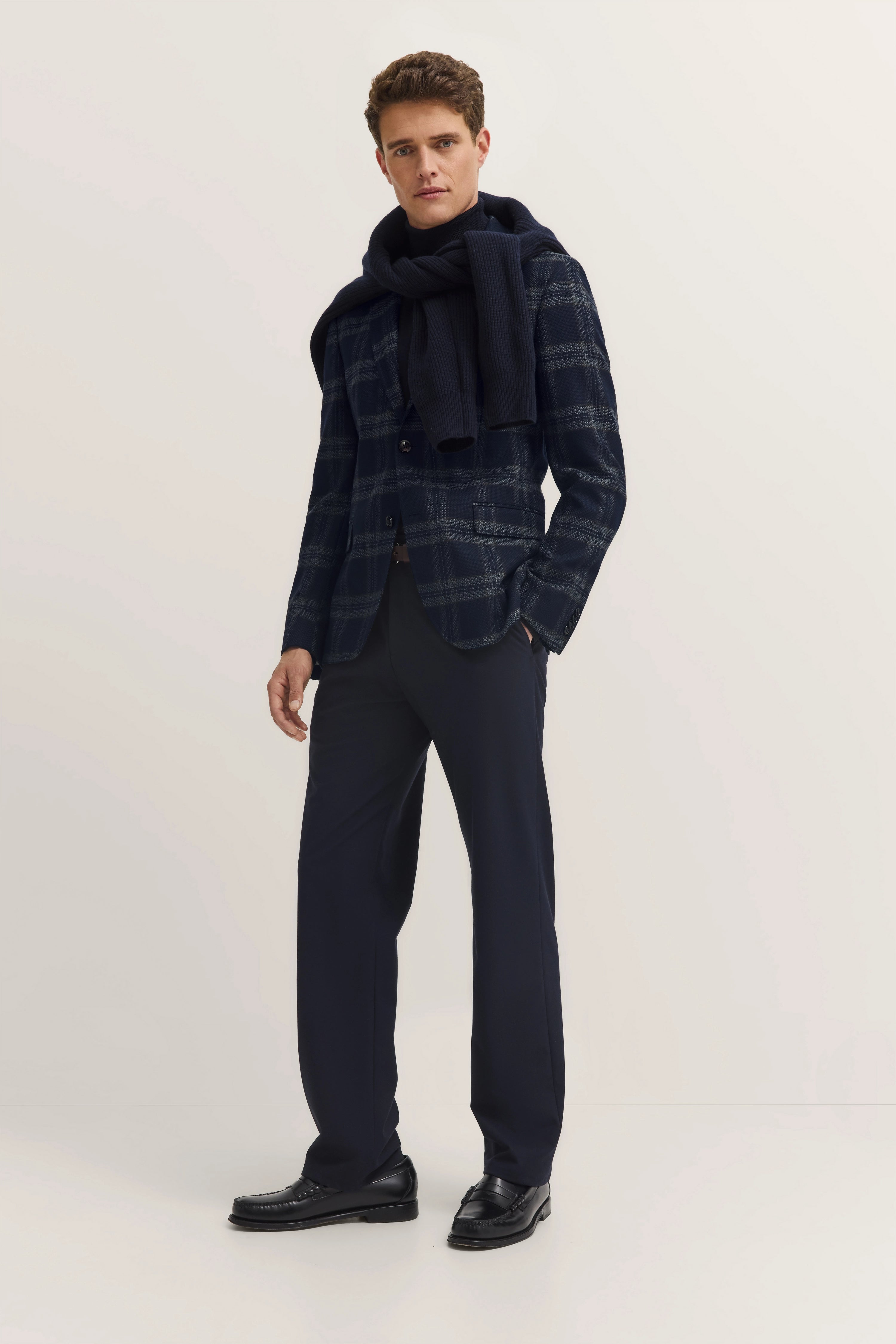 Model in navy checked bugatti blazer, scarf, and trousers, casual pose, stylish and relaxed.