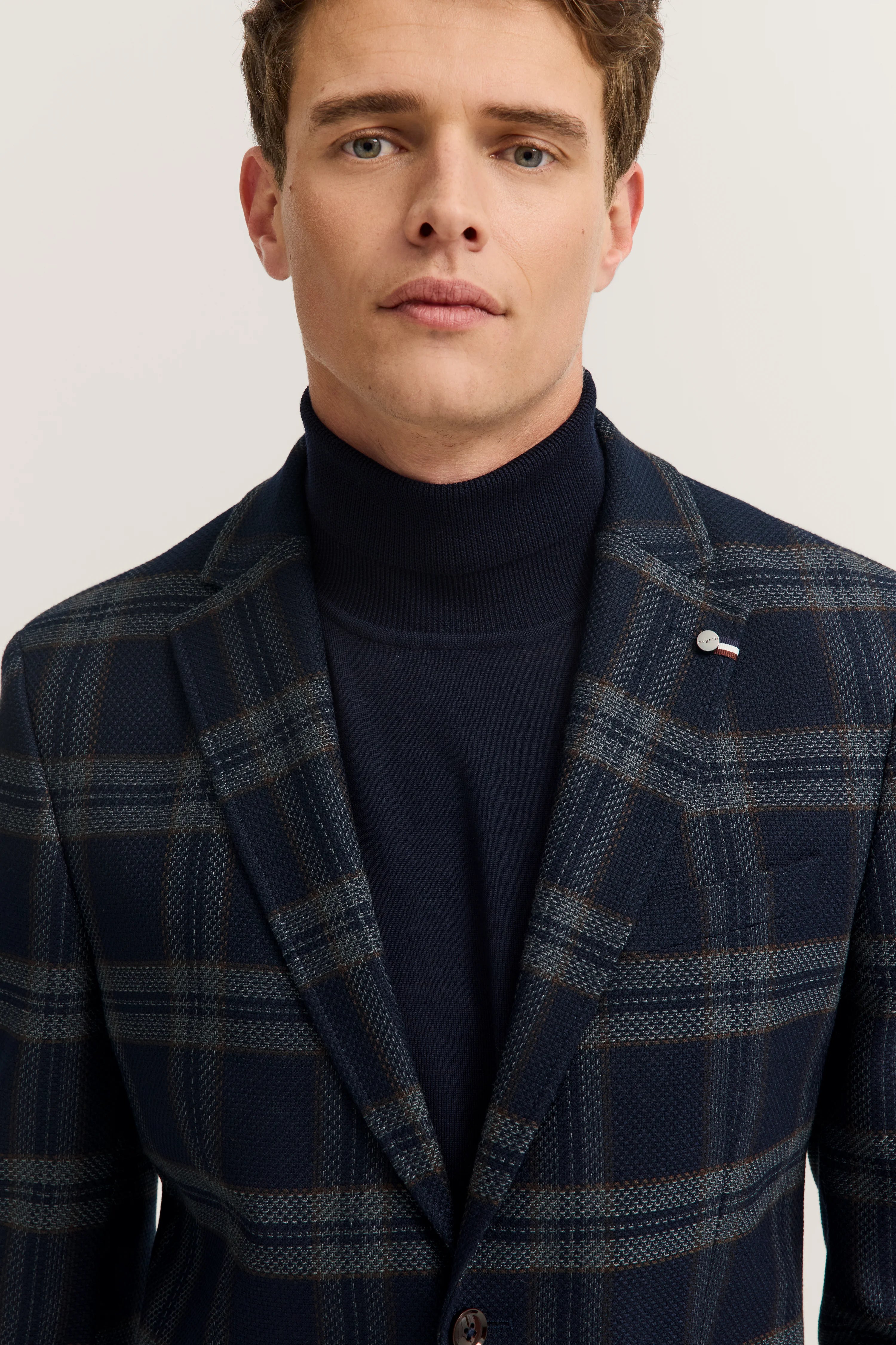 Bust of man in dark blue turtleneck and checkered bugatti blazer.