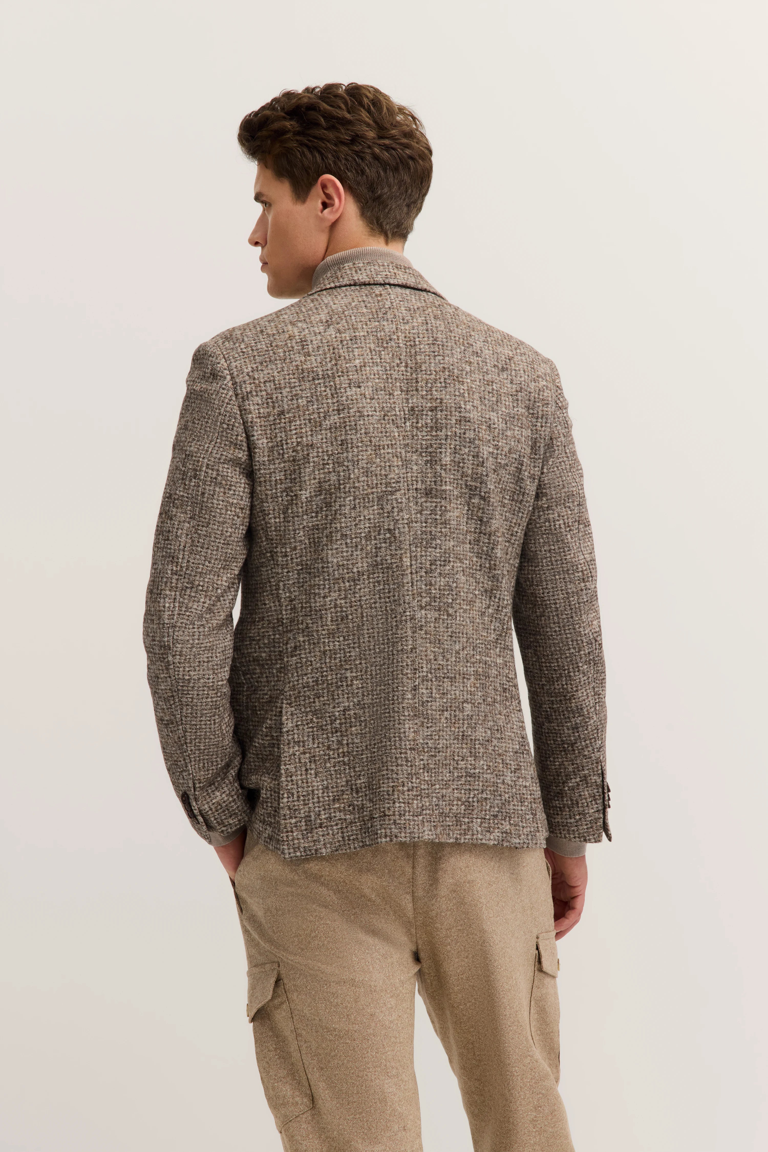 Mann trägt braunen Tweed-Blazer und beige Hose, Rückansicht, legeres Modelbild.