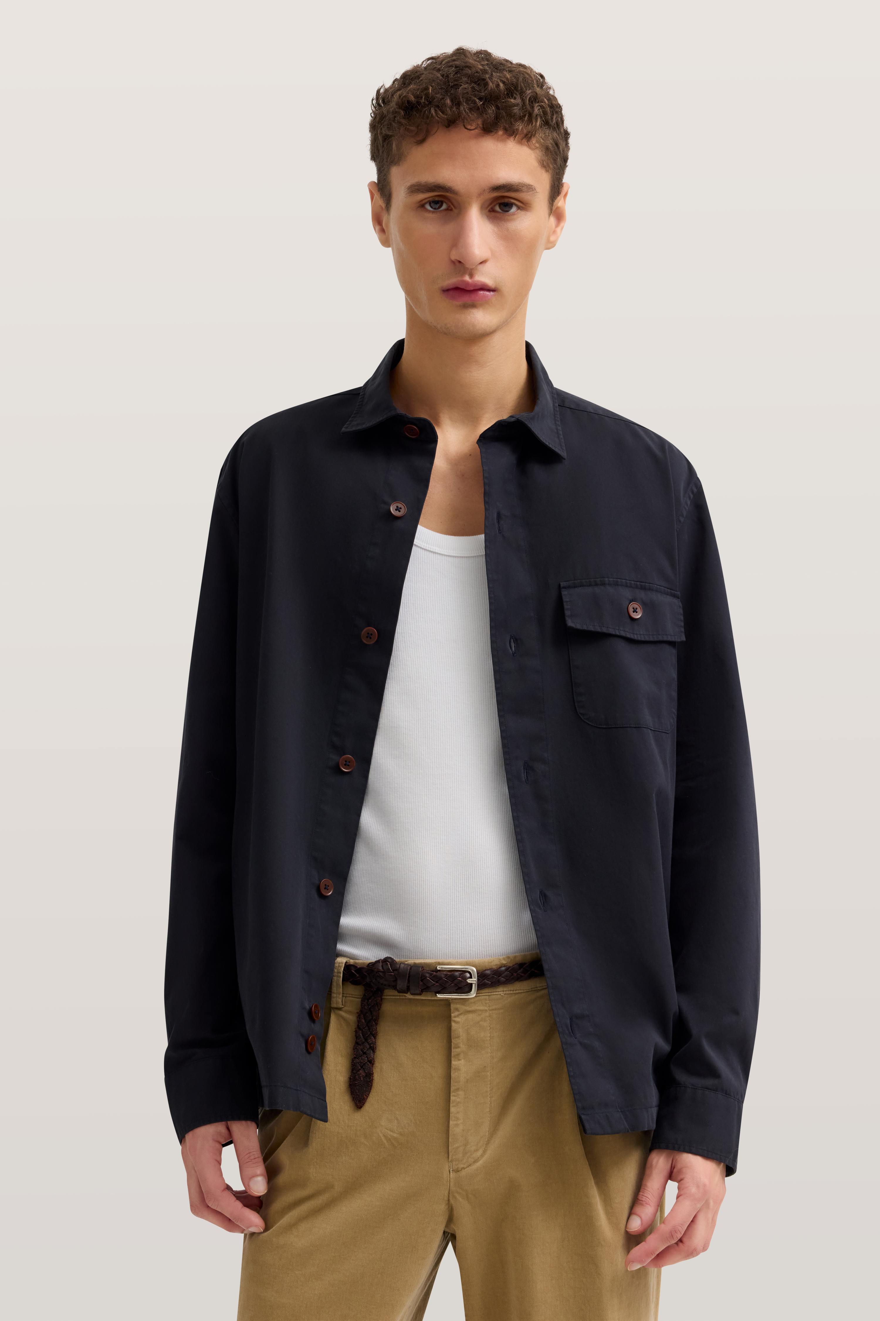 Model trägt bugatti: schwarzes Hemd, weißes Shirt, beige Hose