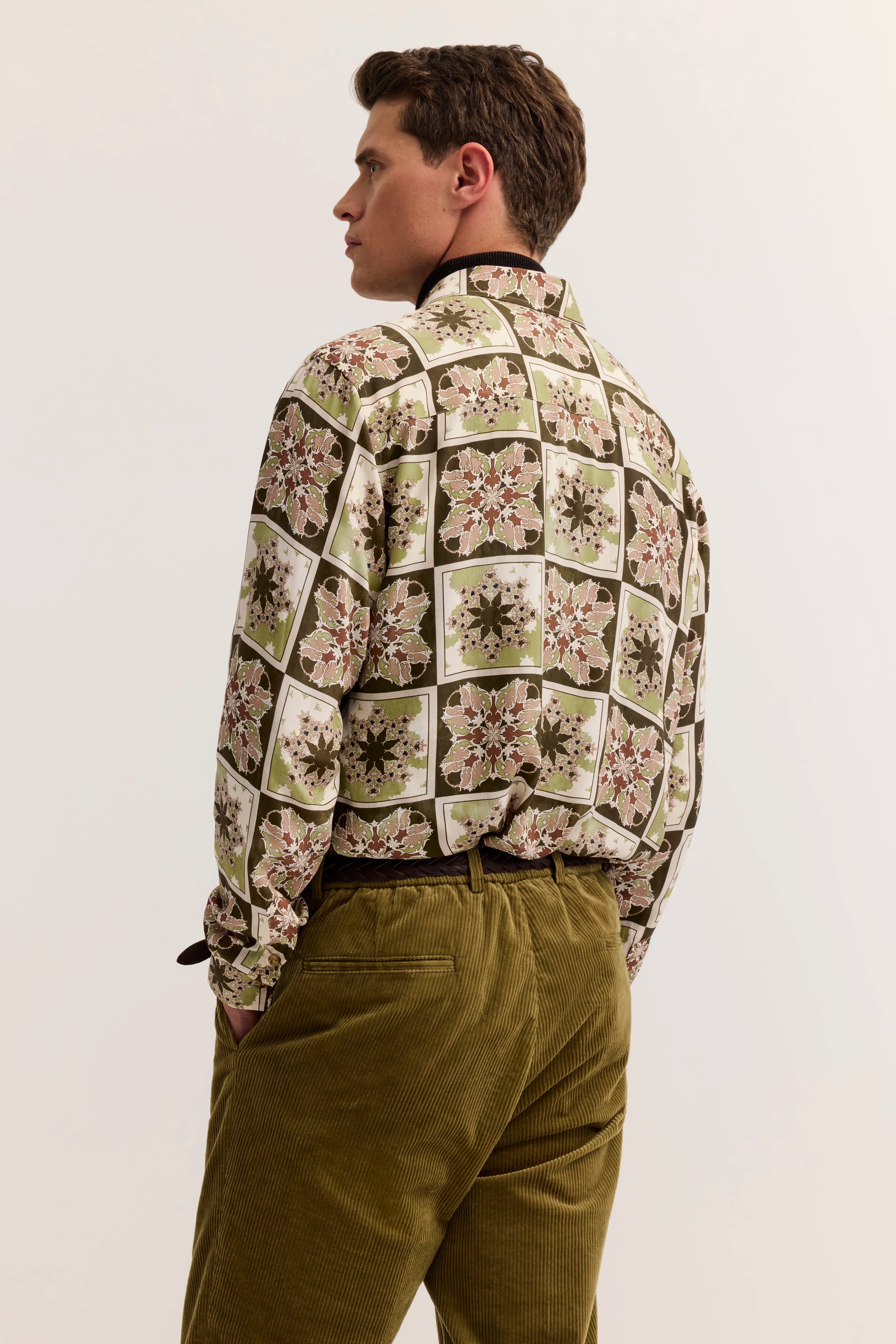 Elegantes bugatti Modelbild: Blumiges Hemd in Grün-Beige, Cordhose in Oliv, seitlich posiert.