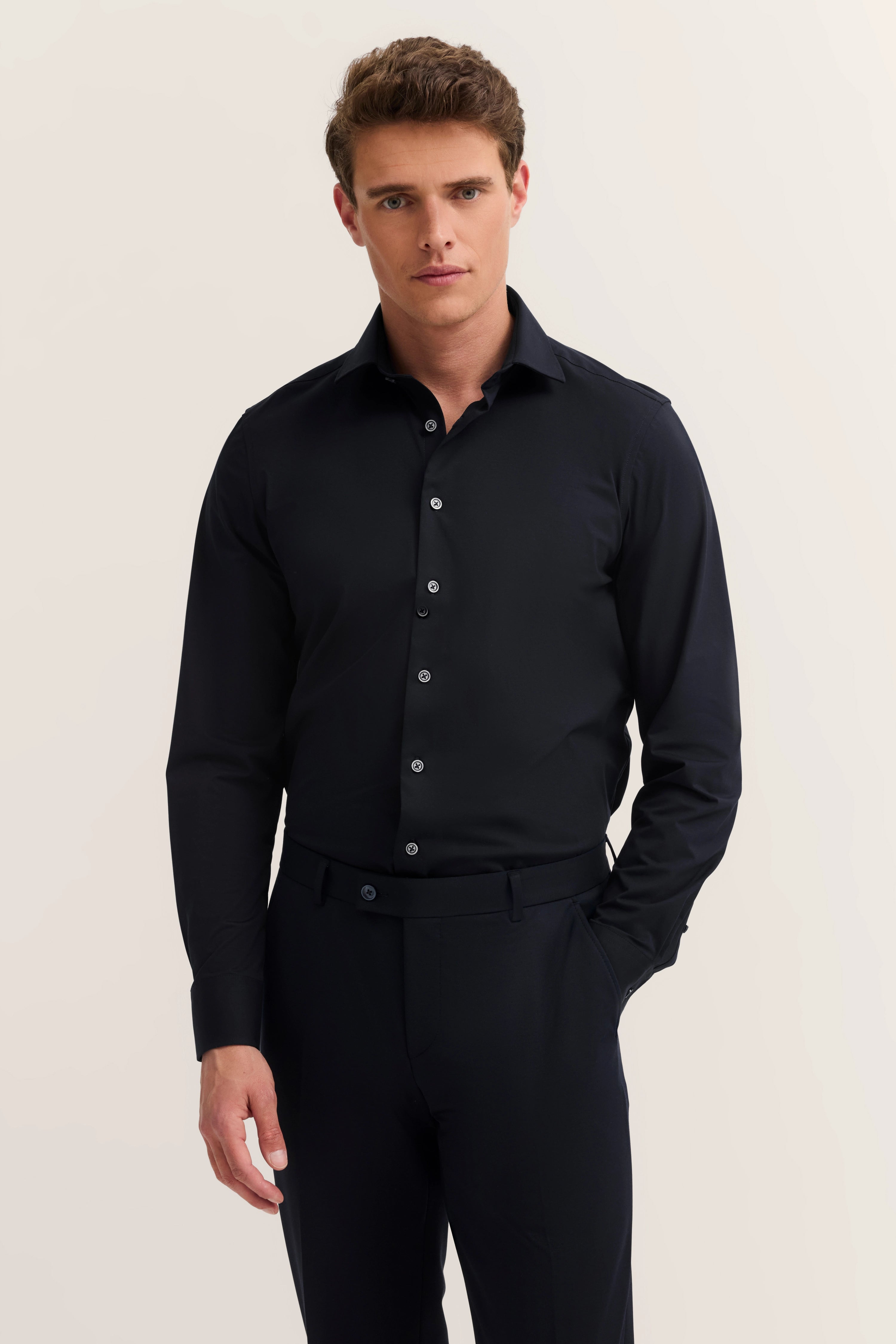 Zwart bugatti-overhemd en broek, modelpose, hand in zak, ontspannen uitstraling.
