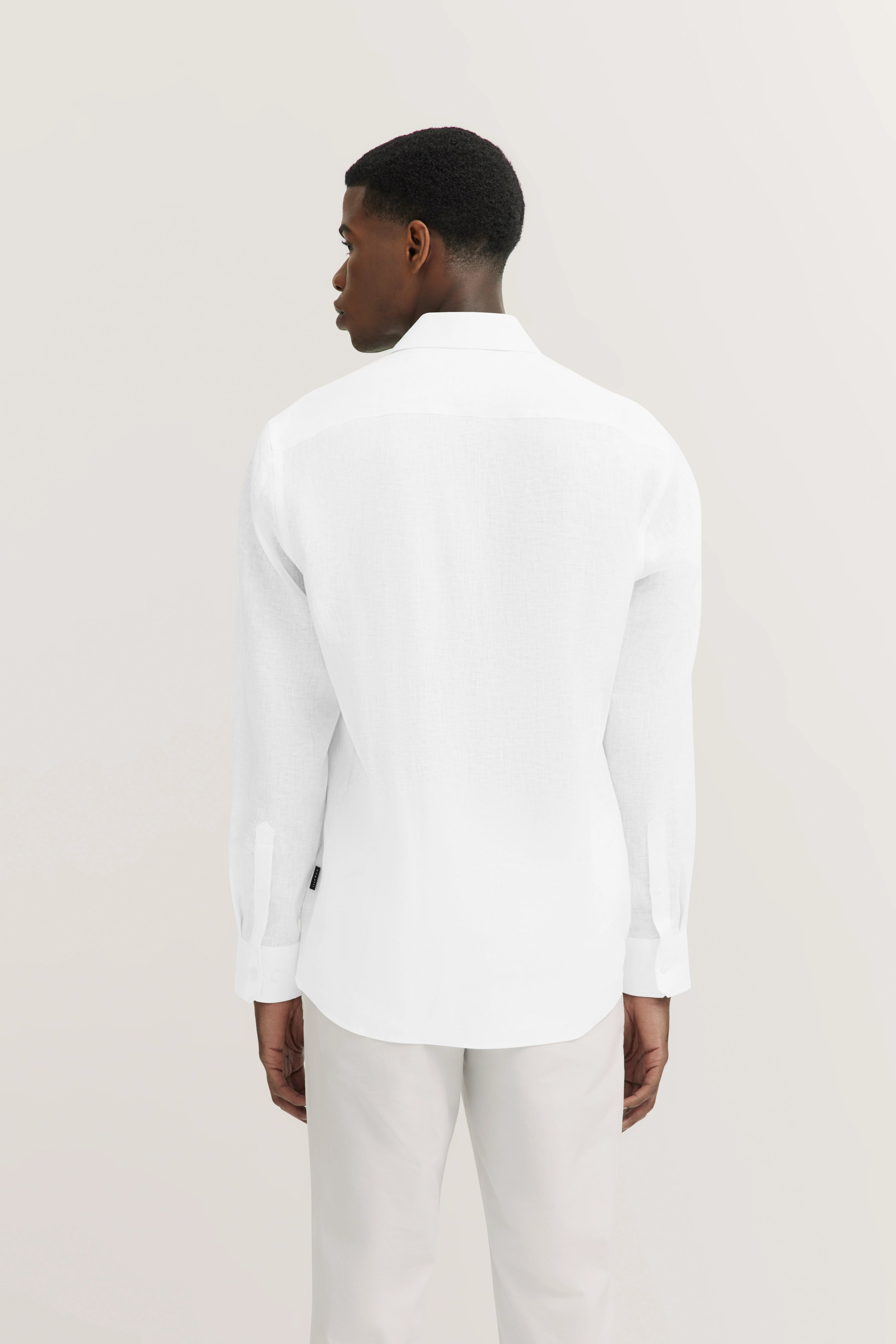 Wit overhemd en lichte broek van achteren, casual model, ontspannen houding.