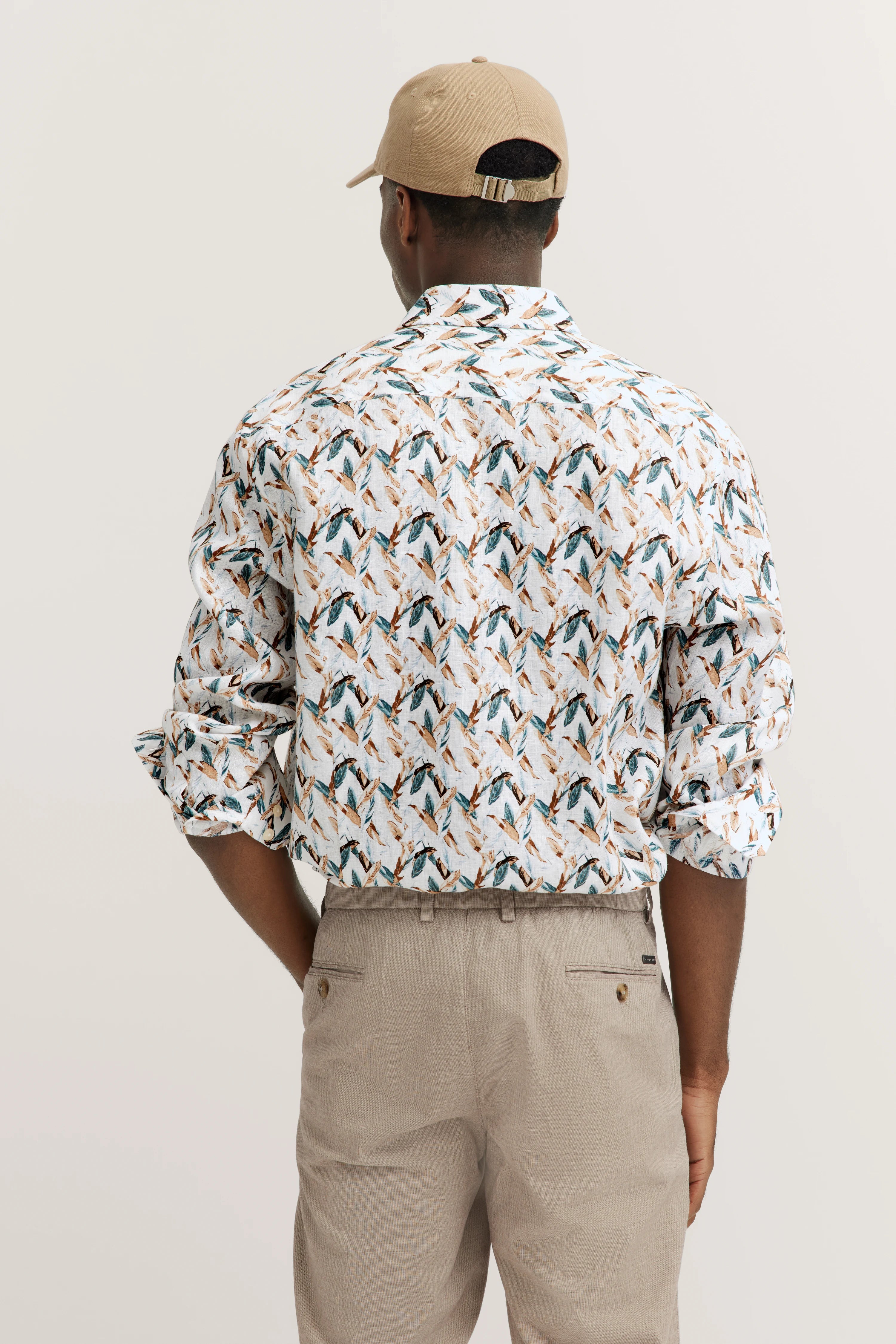 Model in beige broek, beige-blauw patroonhemd, beige hoed, rugaanzicht.