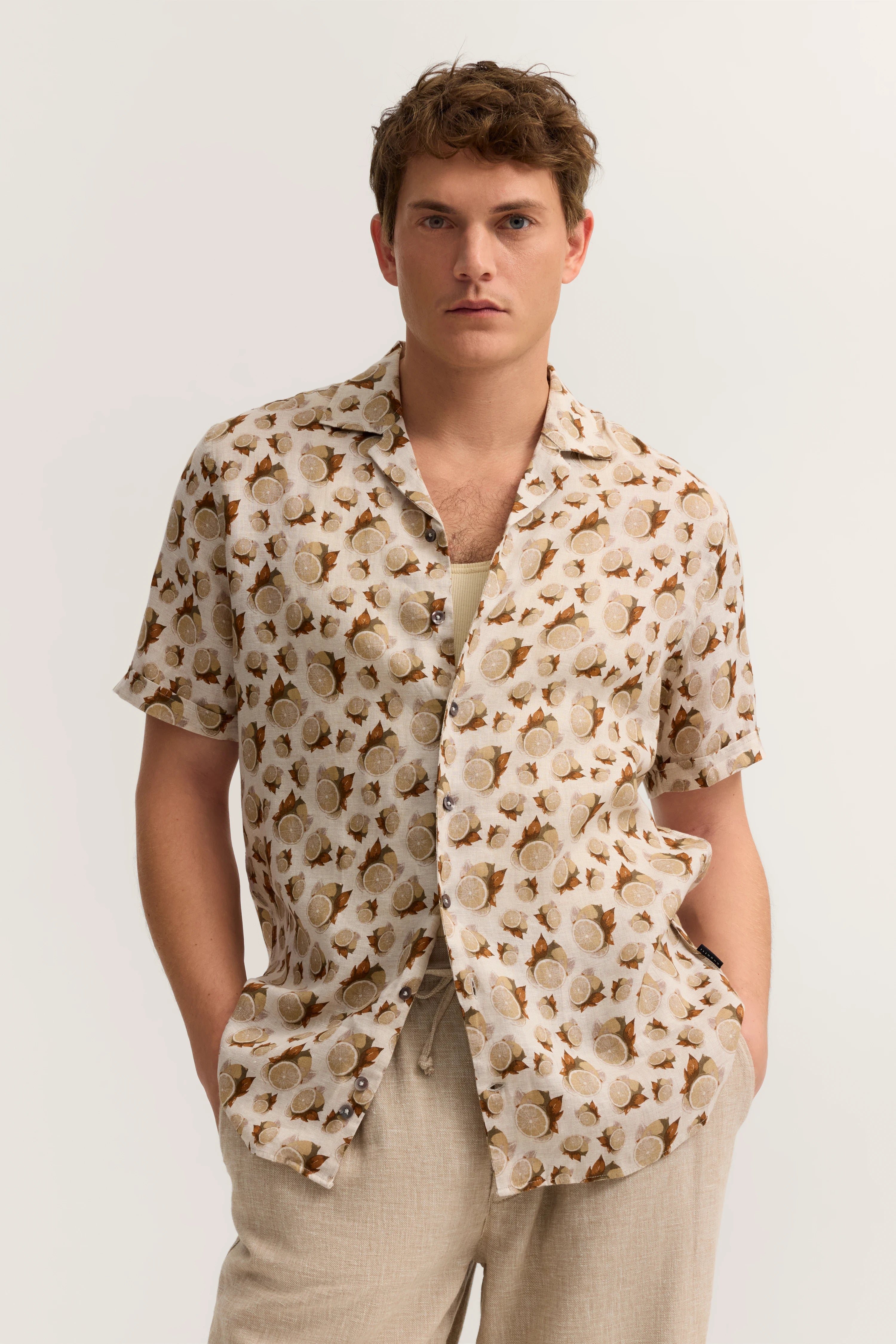Bugatti Modelbild: Beige Hemd mit Blättermuster, helles Top, entspannte Pose, Hände in Taschen.