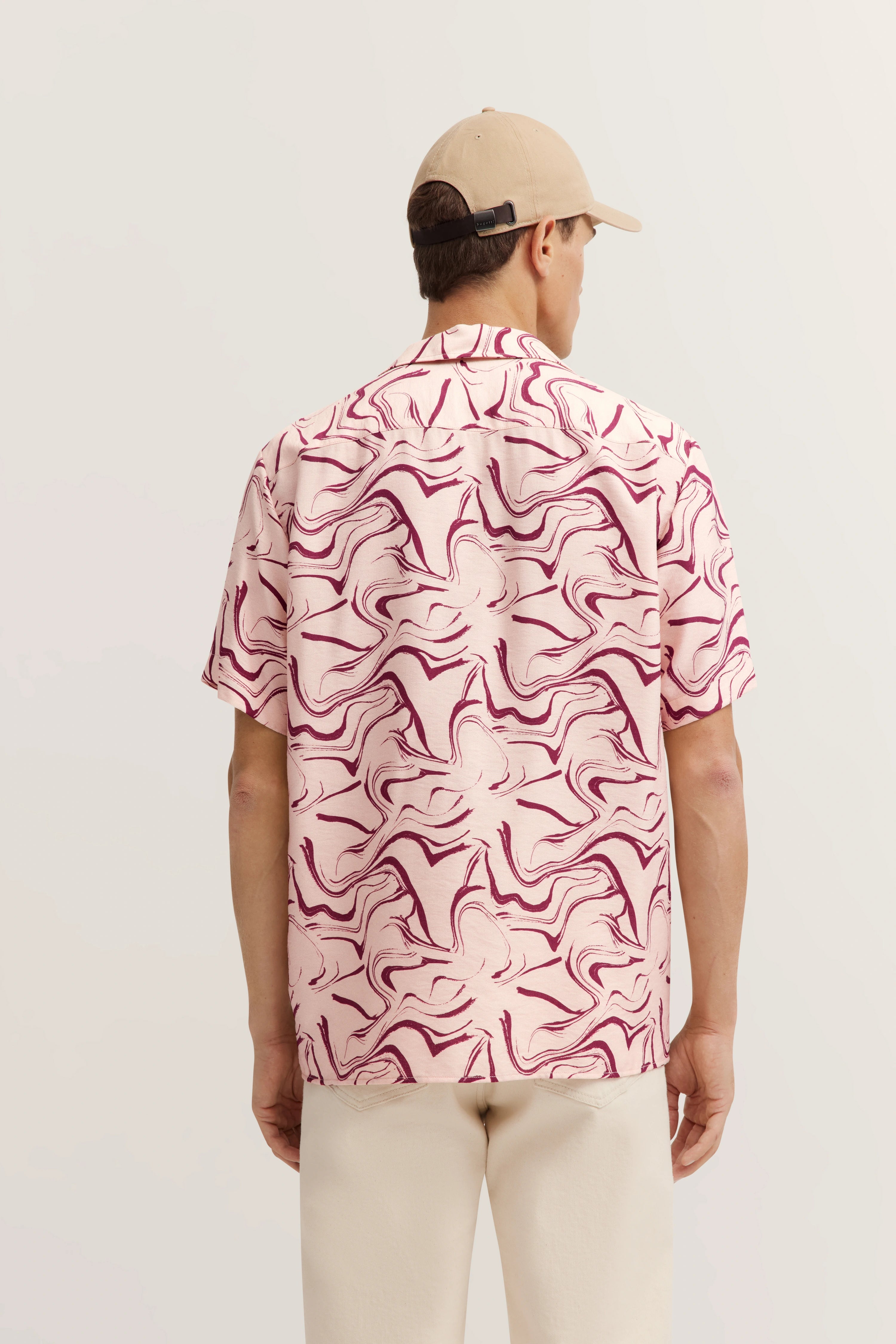 Roze kort mouw overhemd met abstract patroon, beige broek, model van achteren, ontspannen pose.