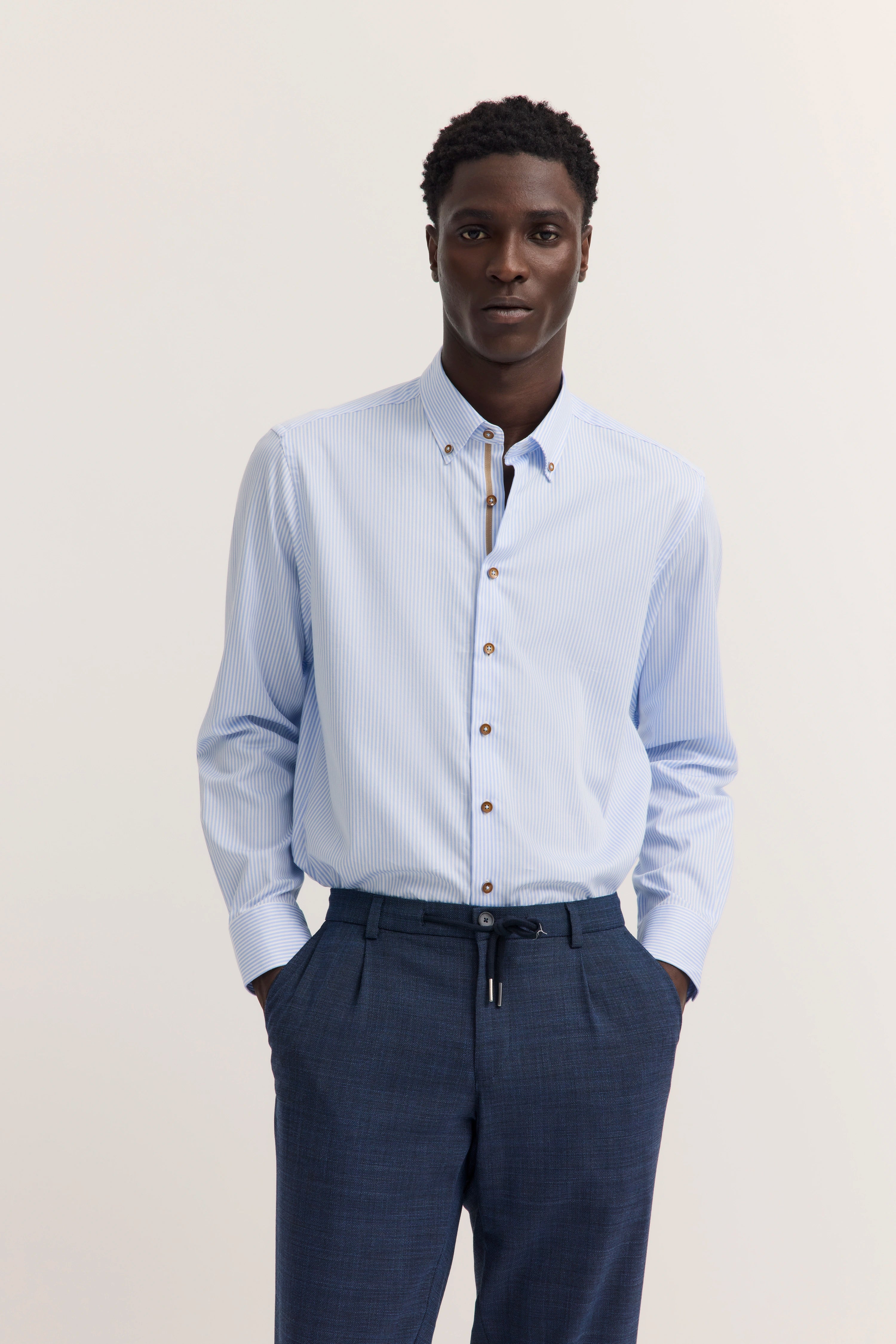 Elegantes Modelbild: Mann im hellblauen Streifenhemd, blaue Hose, Hände in den Hosentaschen.