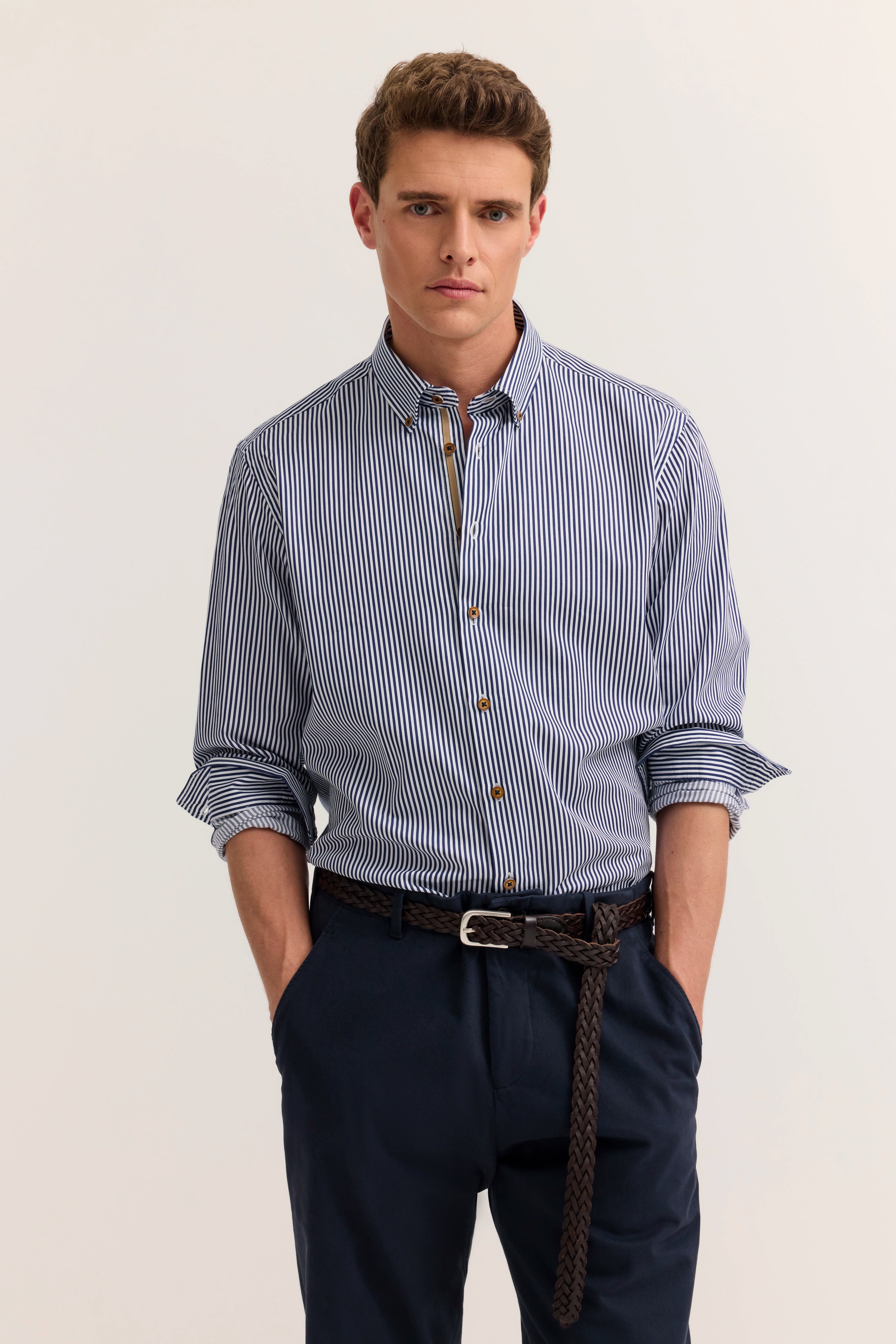 Model in gestreiftem Hemd, blau-weiß, mit hochgekrempelten Ärmeln, dunkler Hose. Bugatti-Stil.