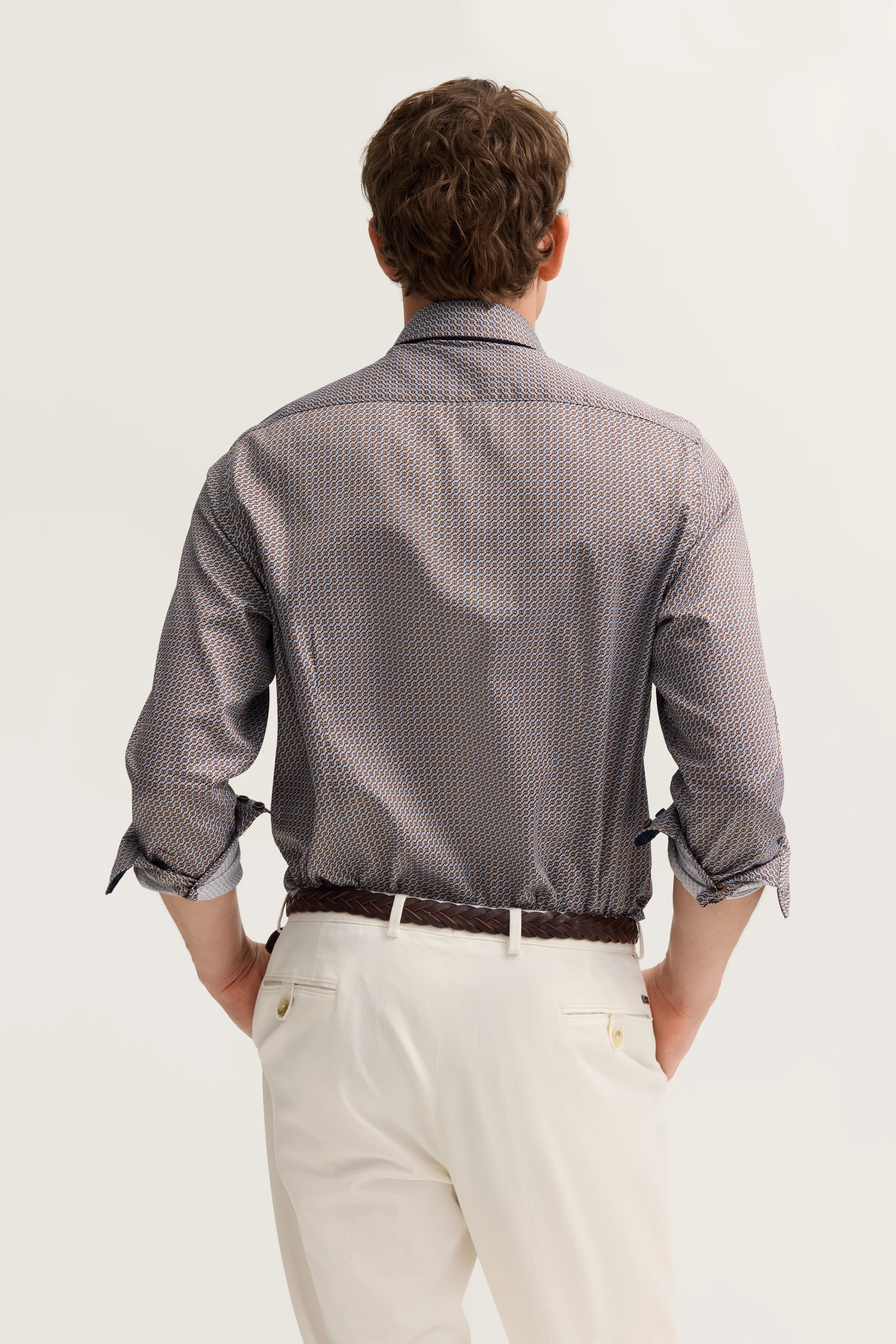Herrenmodell in gemustertem Hemd und weißen Hosen, Rückenansicht, legeres Posing.