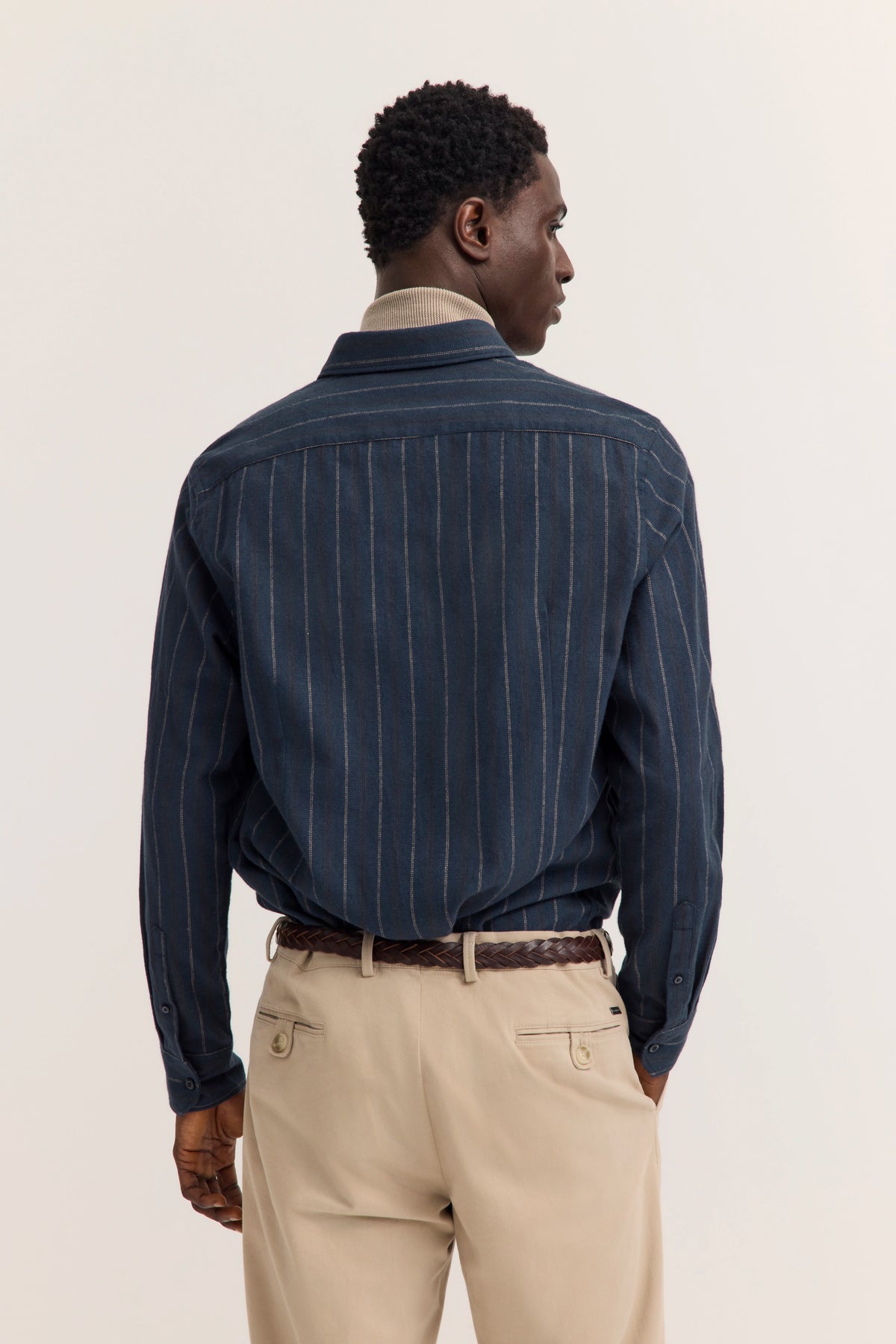 Modelbild: Rückansicht, blau gestreiftes Hemd, beige Hose, lässige Pose.