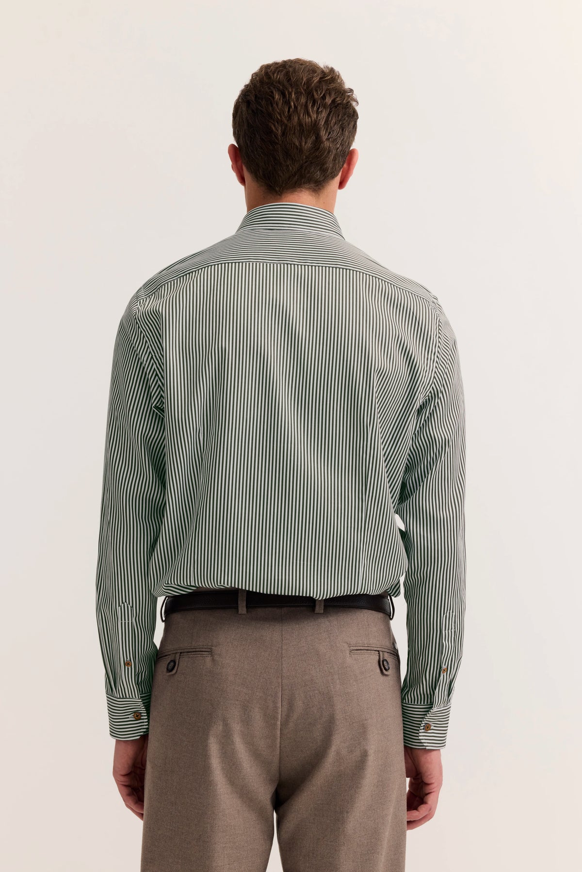 Rückansicht eines Models mit gestreiftem Hemd in Grün und weiß, braune Hose, legeres Outfit.
