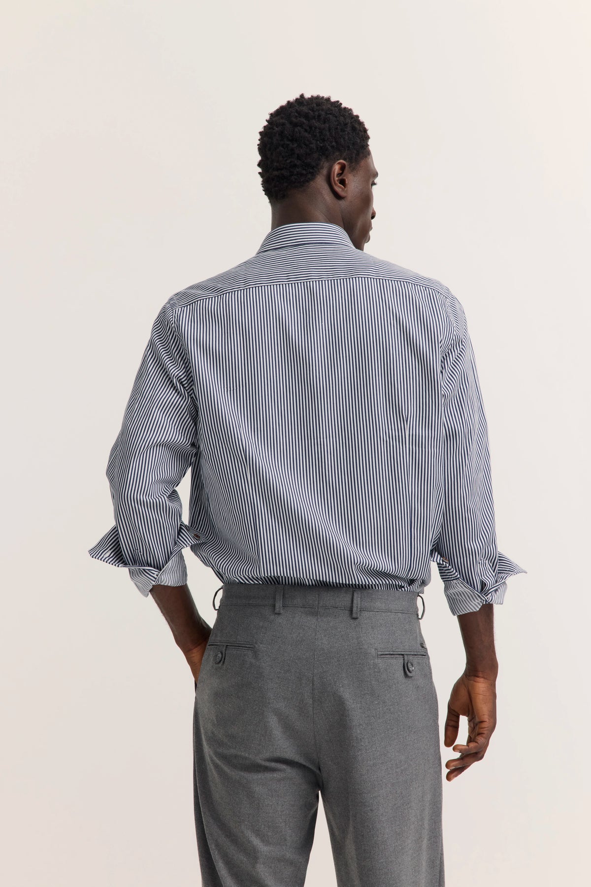 Klassisches Herrenoutfit mit gestreiftem Hemd und grauer Hose von hinten, legeres Modelbild.