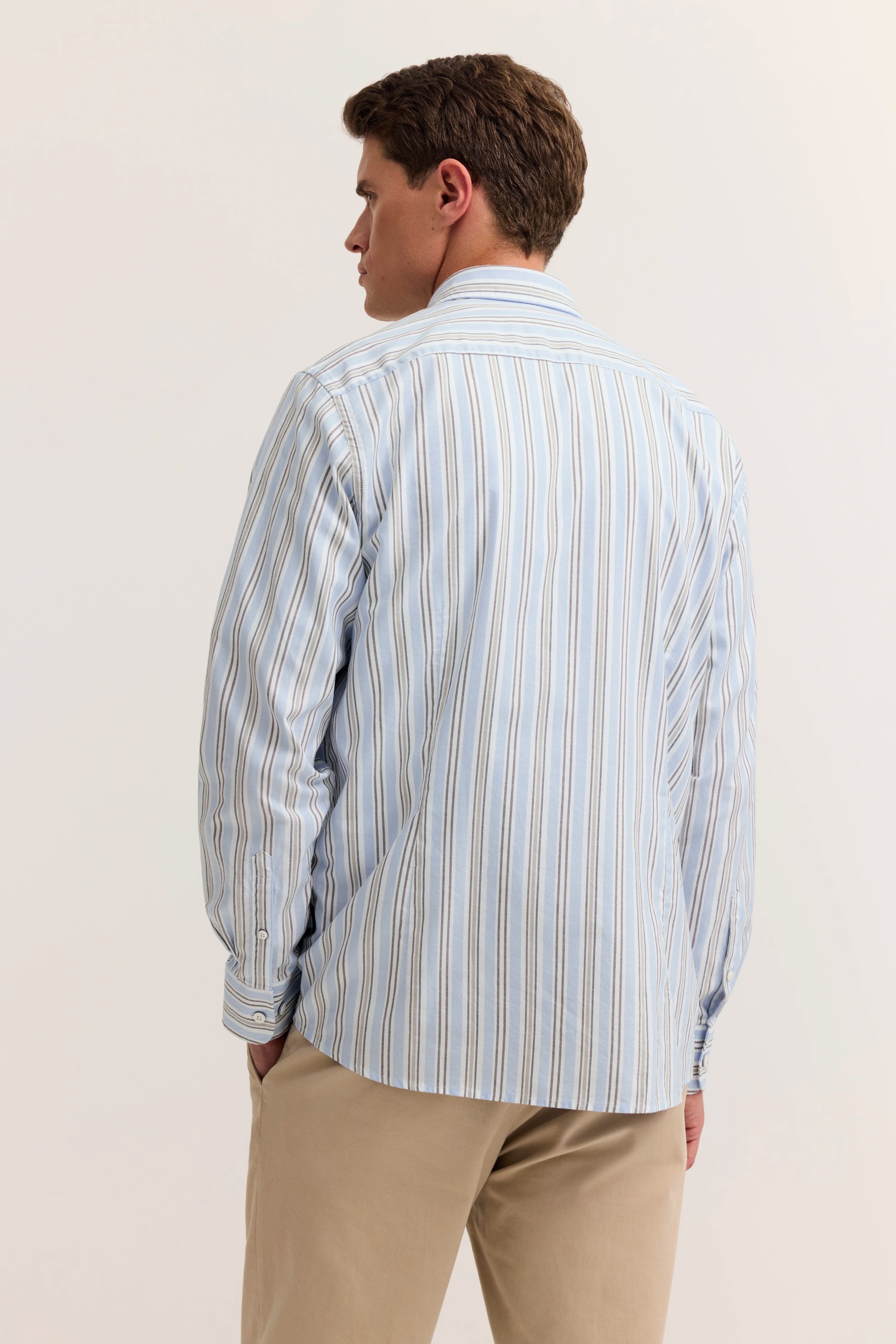 Gestreiftes Hemd in Blau und Weiß, Model von hinten in legerer Pose, beige Hose.