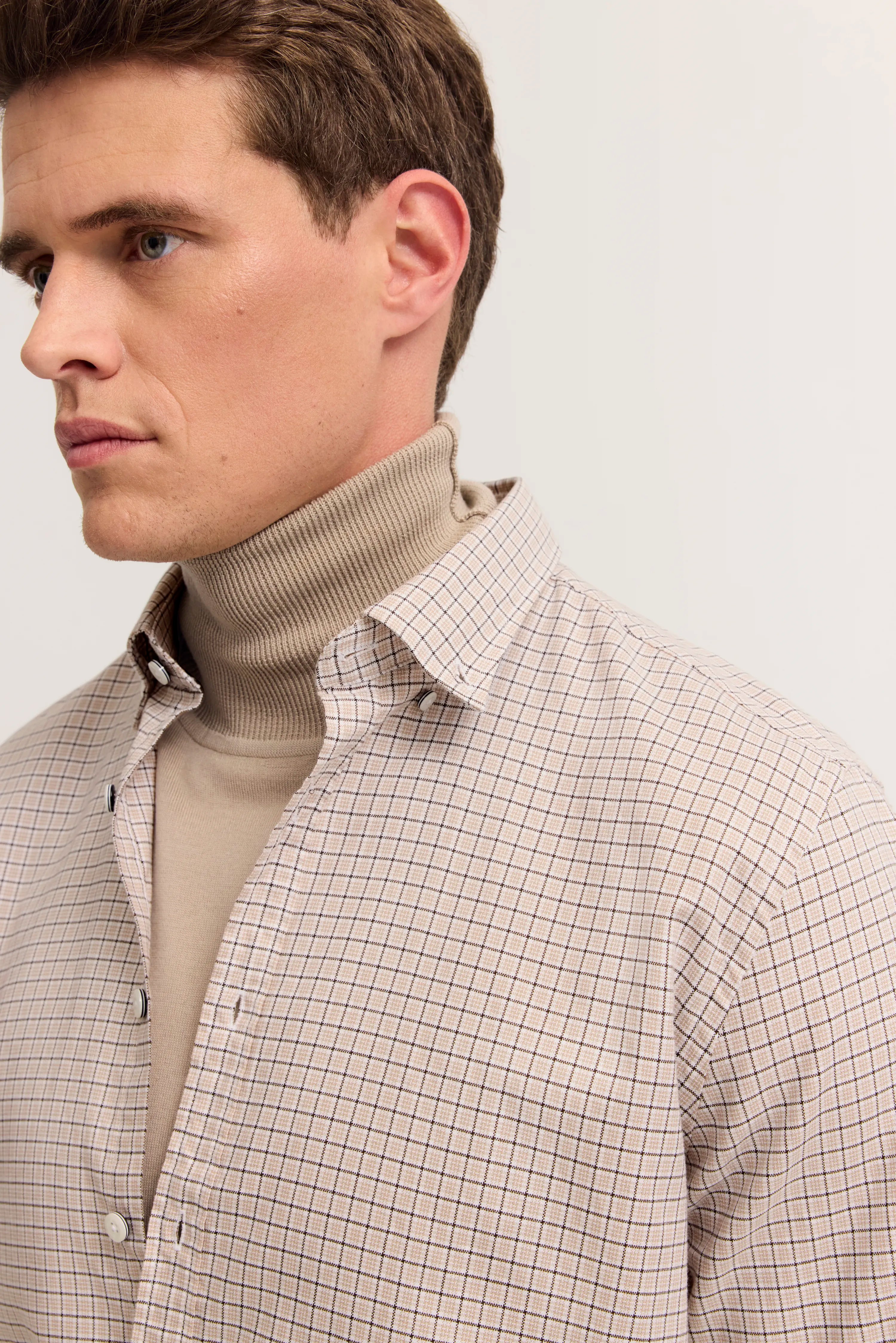 Beiges Rollkragenpullover unter kariertem Hemd, Büstenbild.