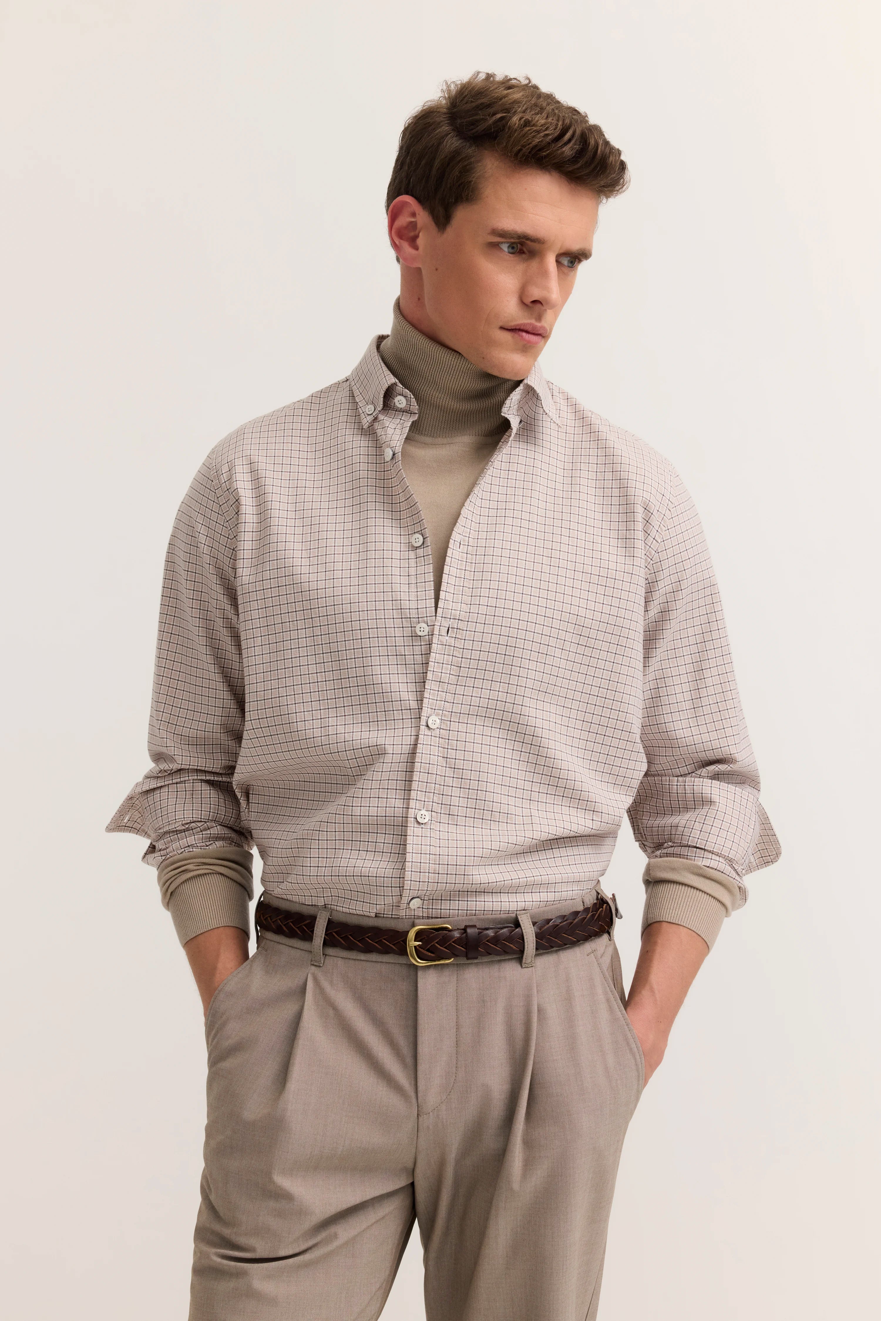 Herren-Outfit mit kariertem Hemd, Rollkragenpullover in Beige und beigefarbener Hose, Model stehend.