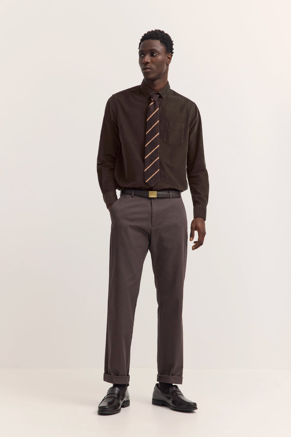Braunes Hemd mit gestreifter Krawatte und grauer Hose, Model steht aufrecht. Bugatti Stil.