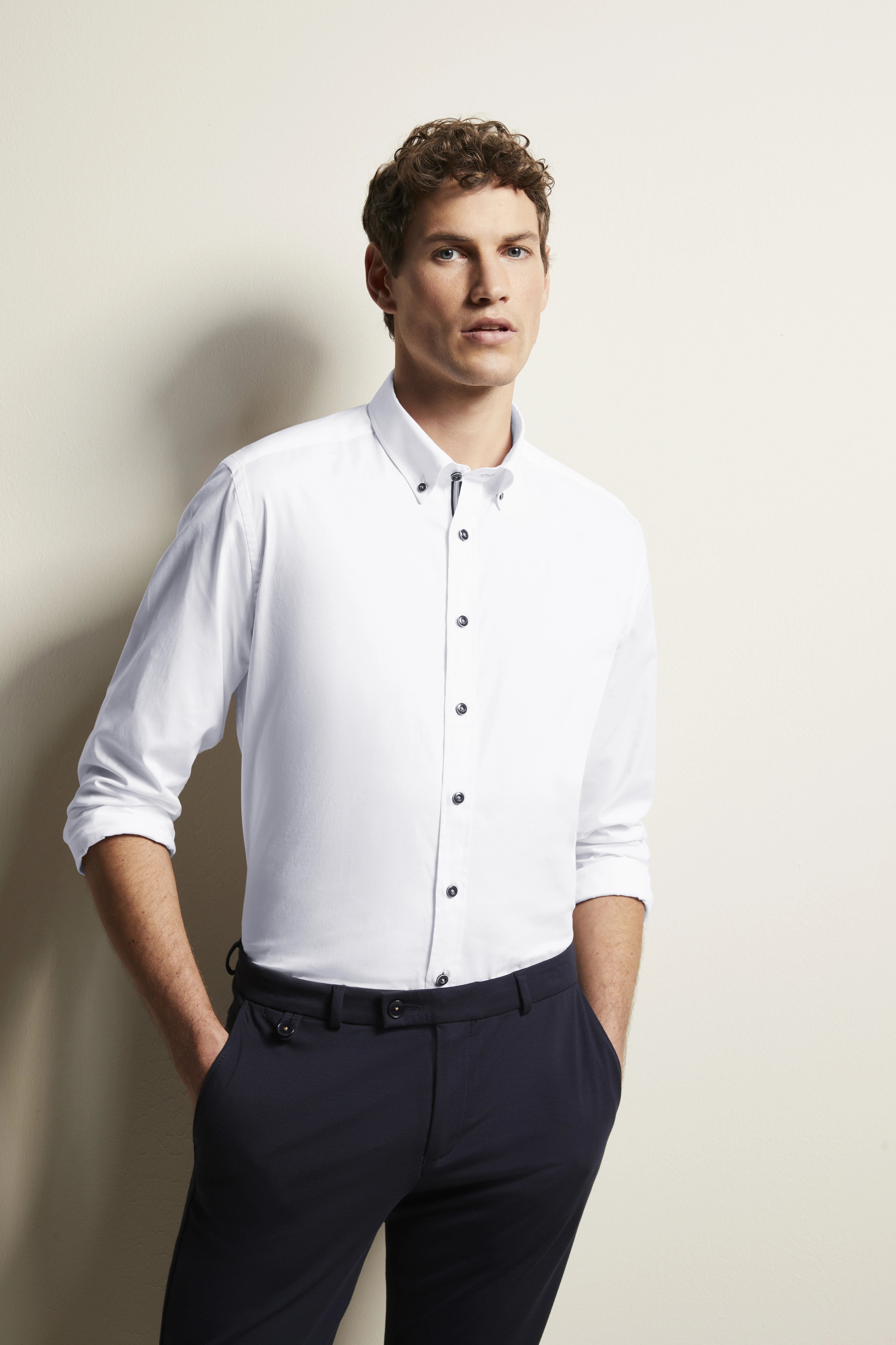 Weiße bugatti Hemd, dunkelblaue Hose, Modelbild, lässige Pose mit Händen in Hosentaschen.