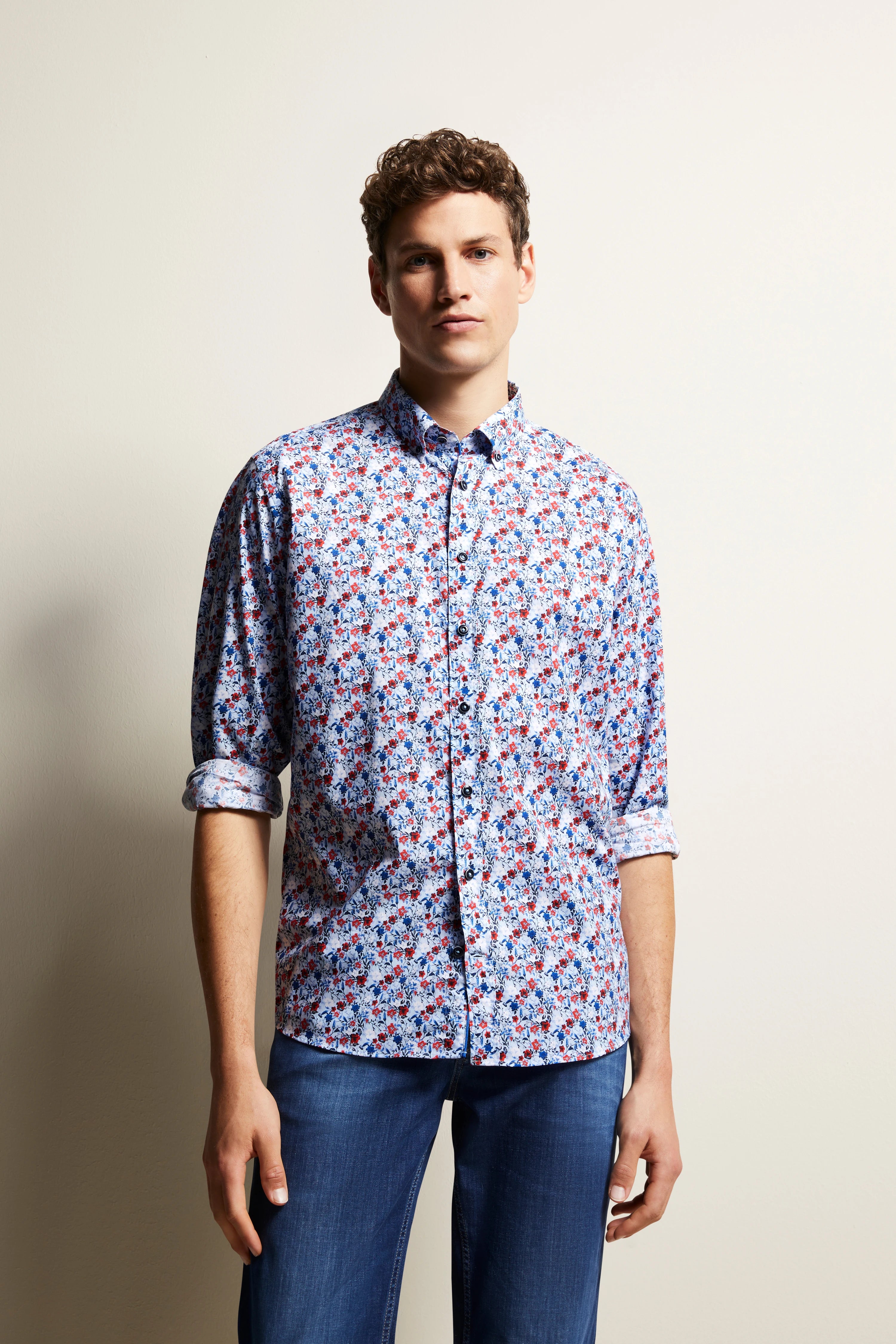bugatti modelafbeelding: Man in bloemenprint overhemd met lange mouwen, blauwe jeans, ontspannen pose.