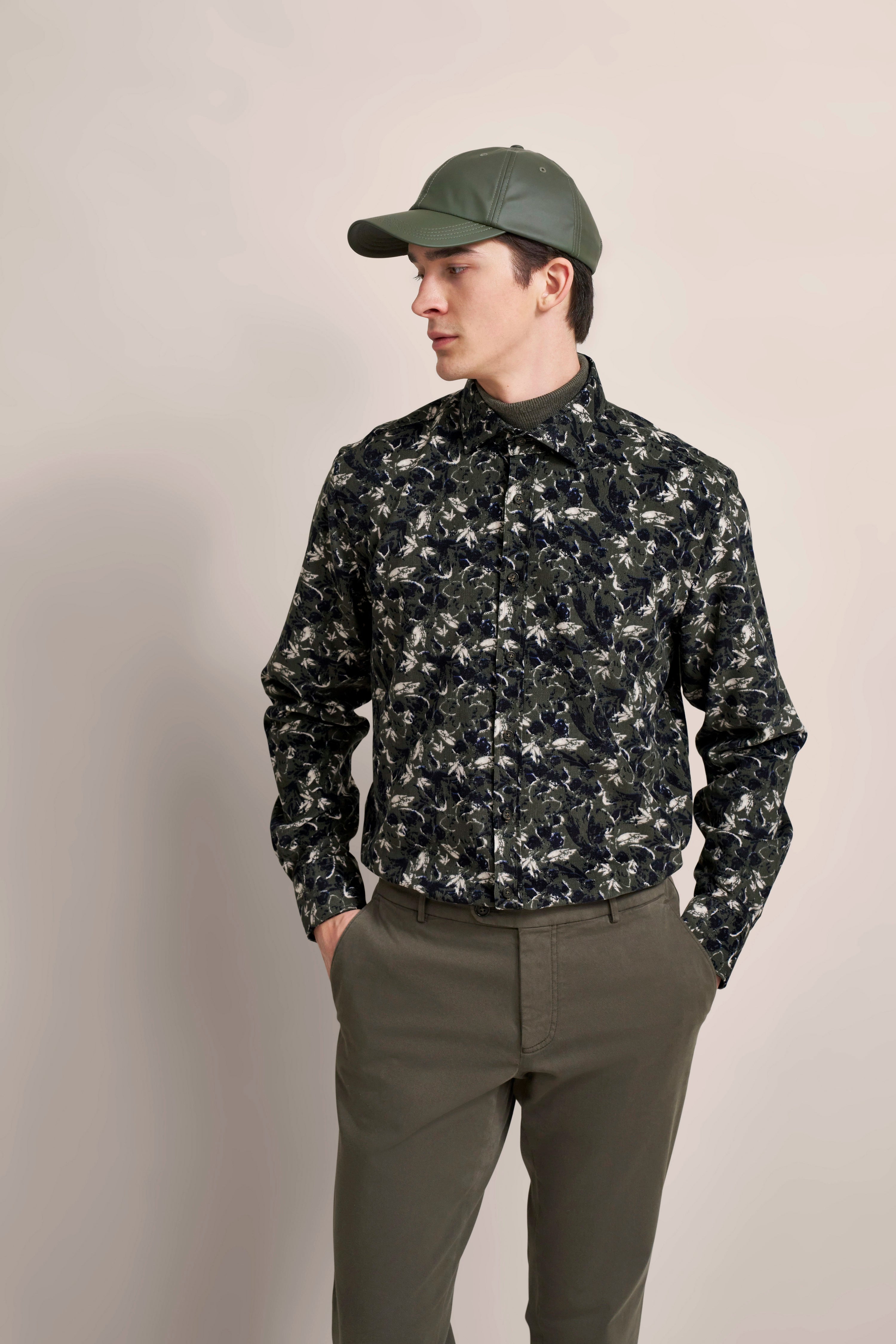 Model in floral Hemd und oliver Hose, Bugatti-Stil, legeres Posing mit grüner Cap.