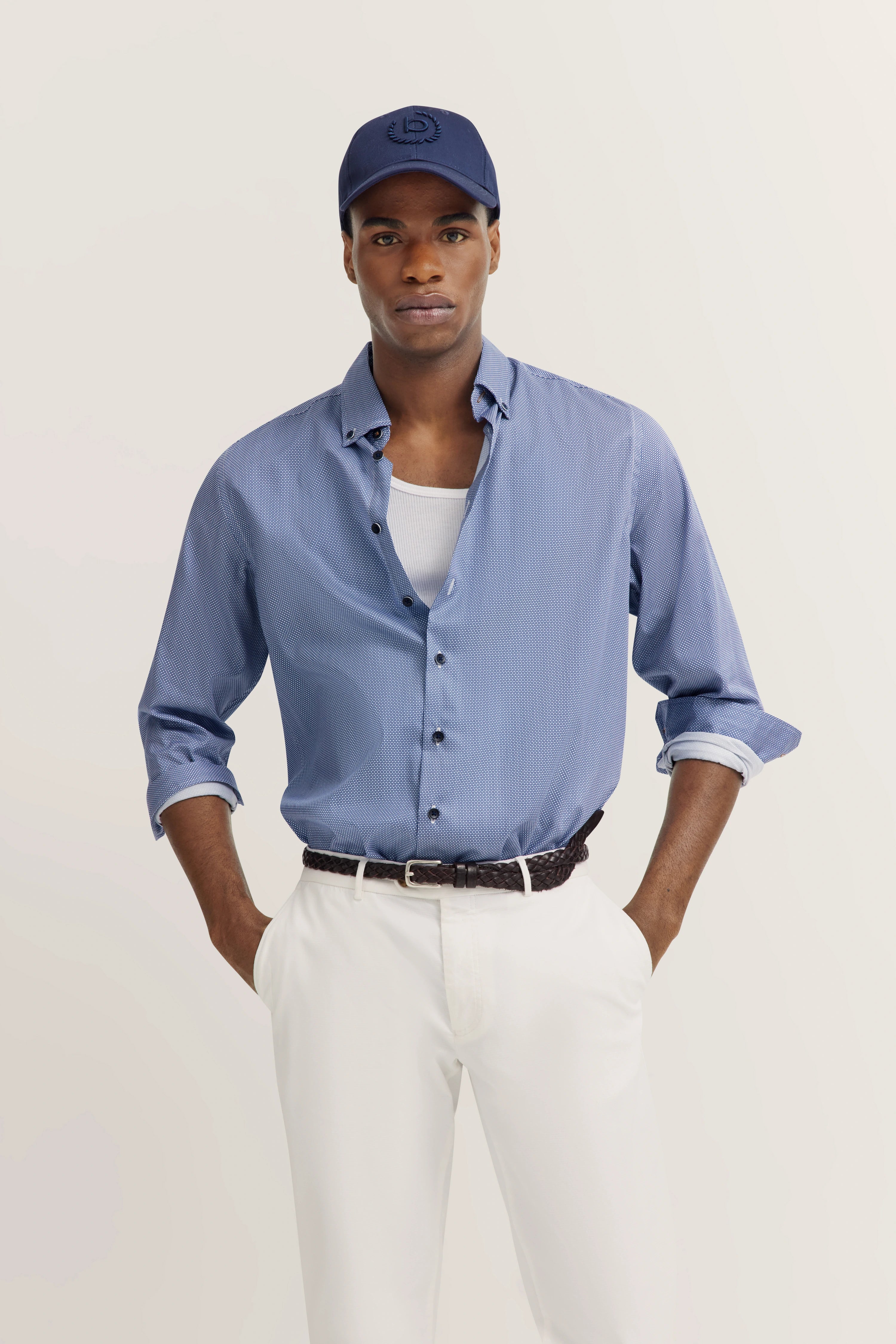 Blau hemd en witte broek, model poseert ontspannen, blauwe pet, bugatti stijl en verfijning.