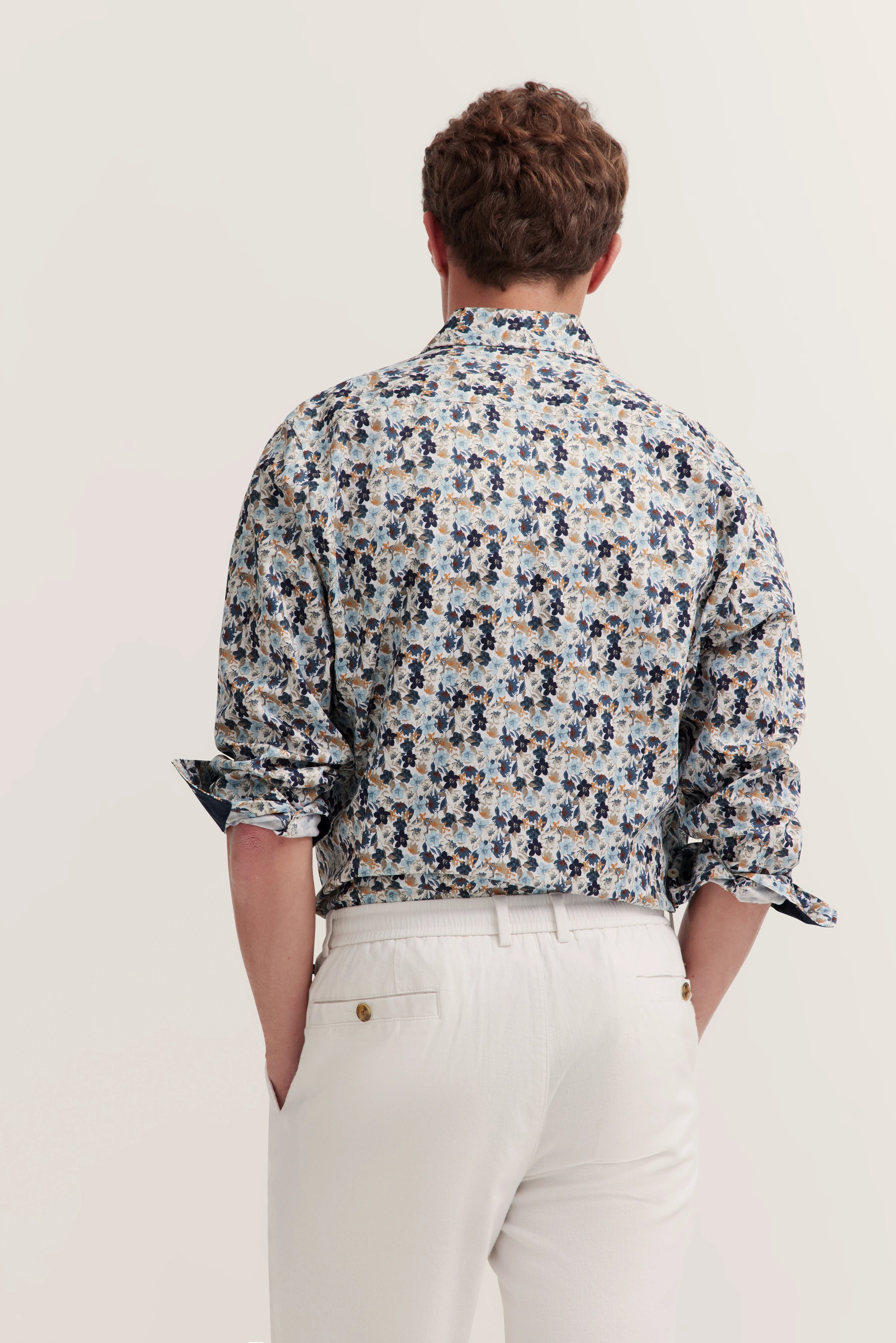 Achterkant van een blauw-wit bloemenhemd van bugatti, gedragen met witte broeken. Model straalt Italiaanse ontspanning uit.