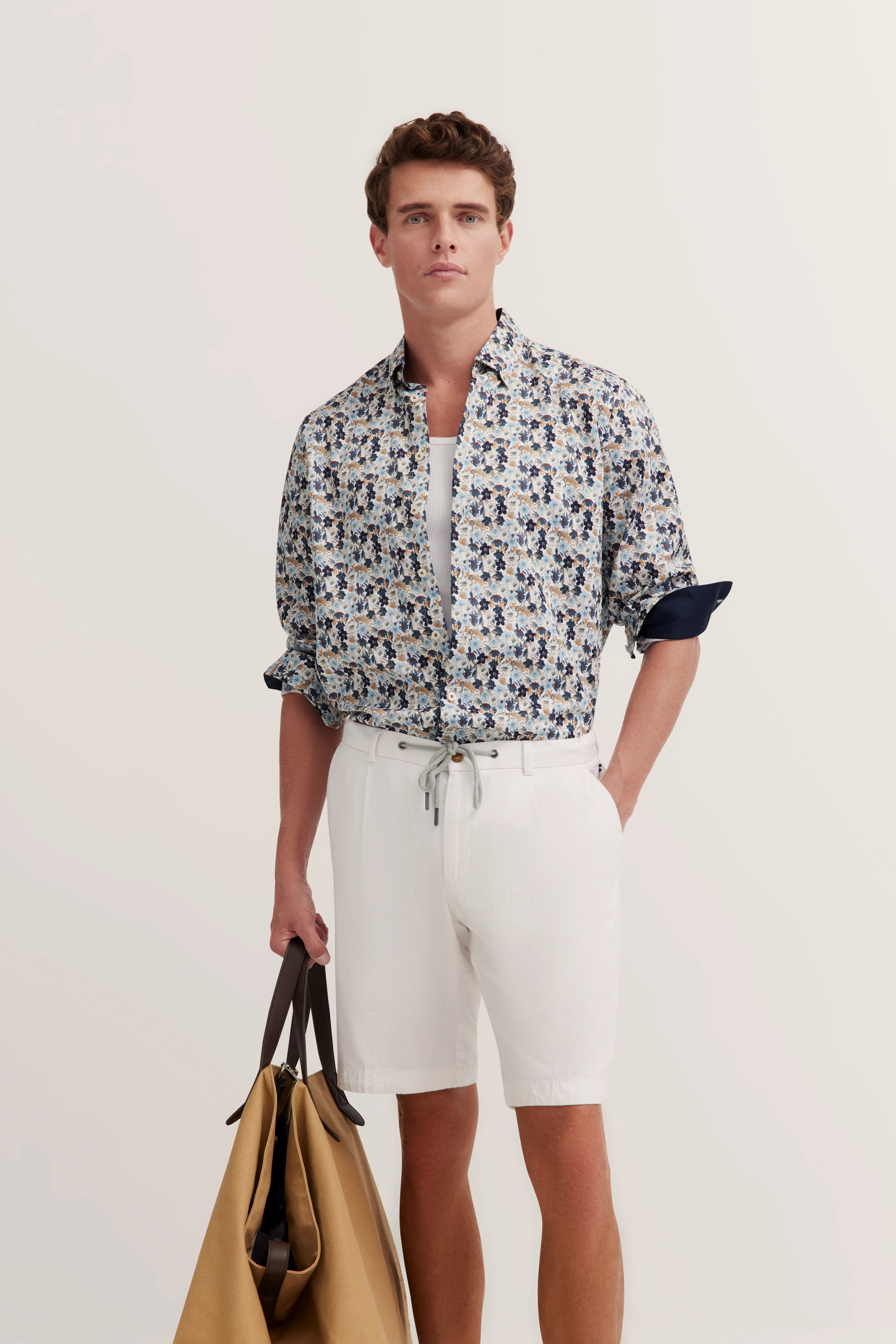 blauw-wit gebloemd overhemd, witte shorts, model met tas, ontspannen pose.