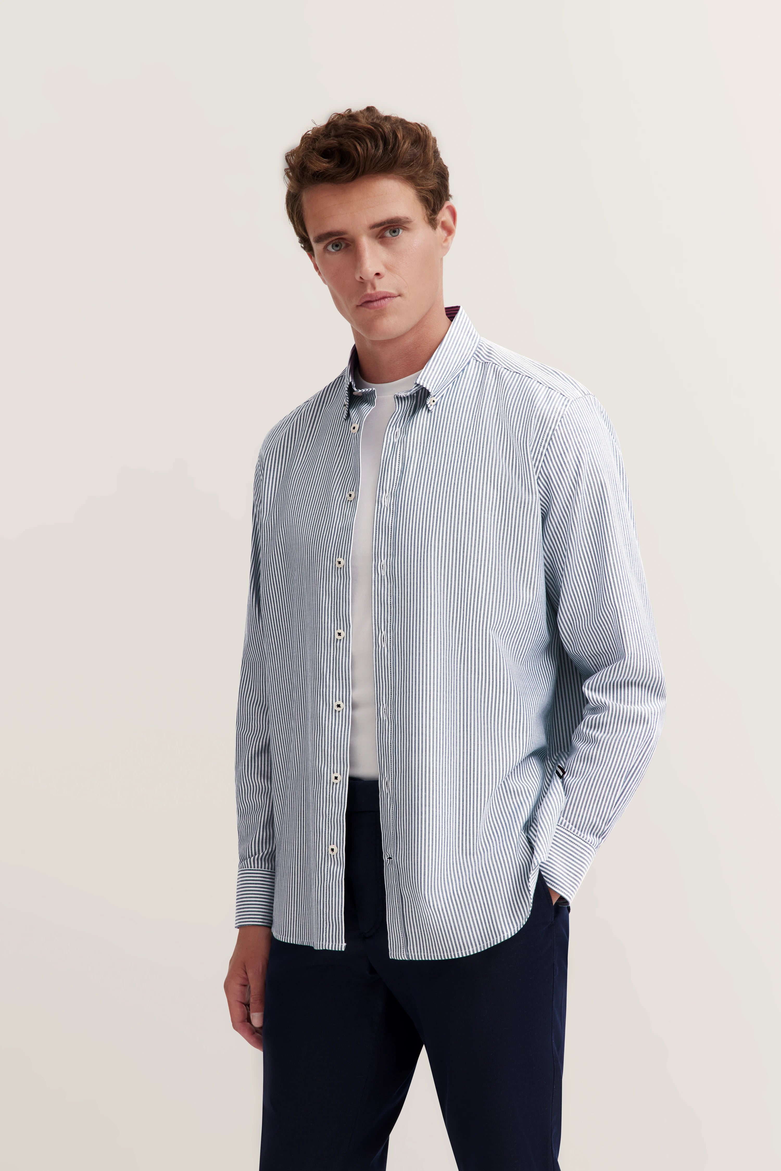 Model draagt gestreept overhemd, wit T-shirt, blauwe broek. Ontspannen pose. bugatti stijl.