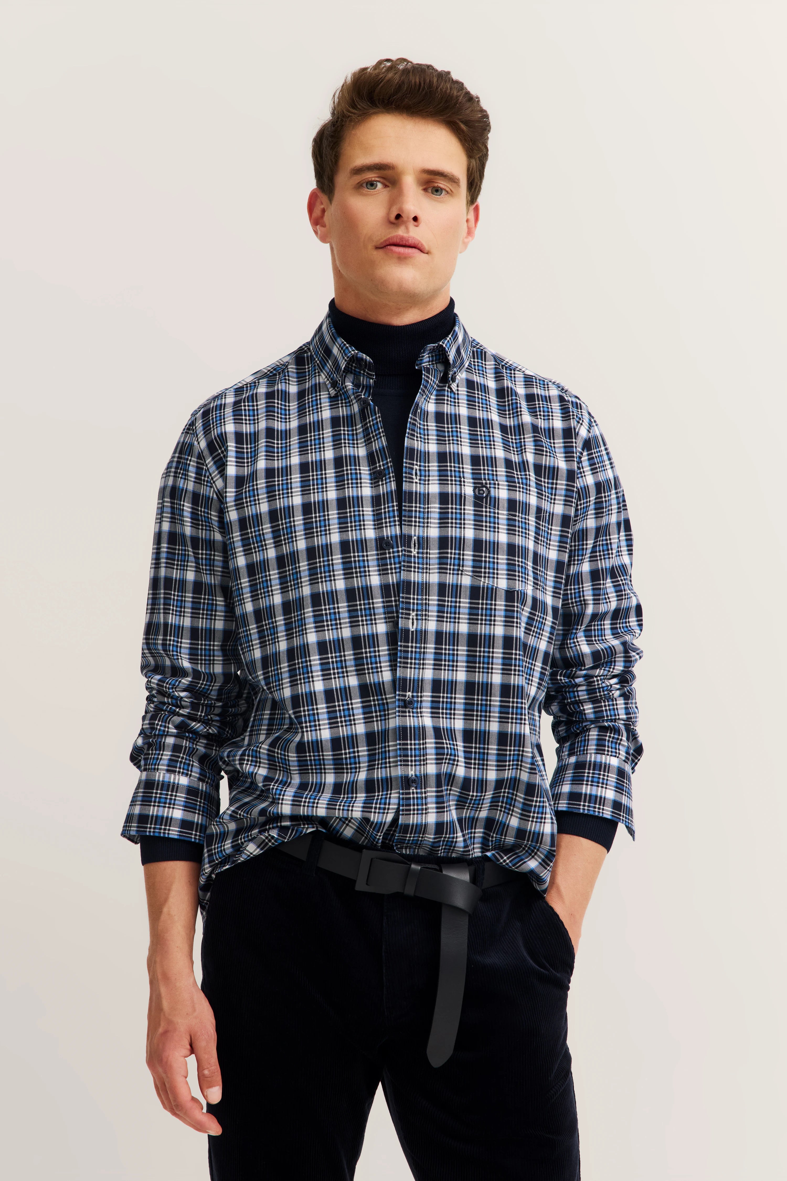 Model in blau-kariertem bugatti Hemd und schwarzem Rollkragenpullover, leger posierend.