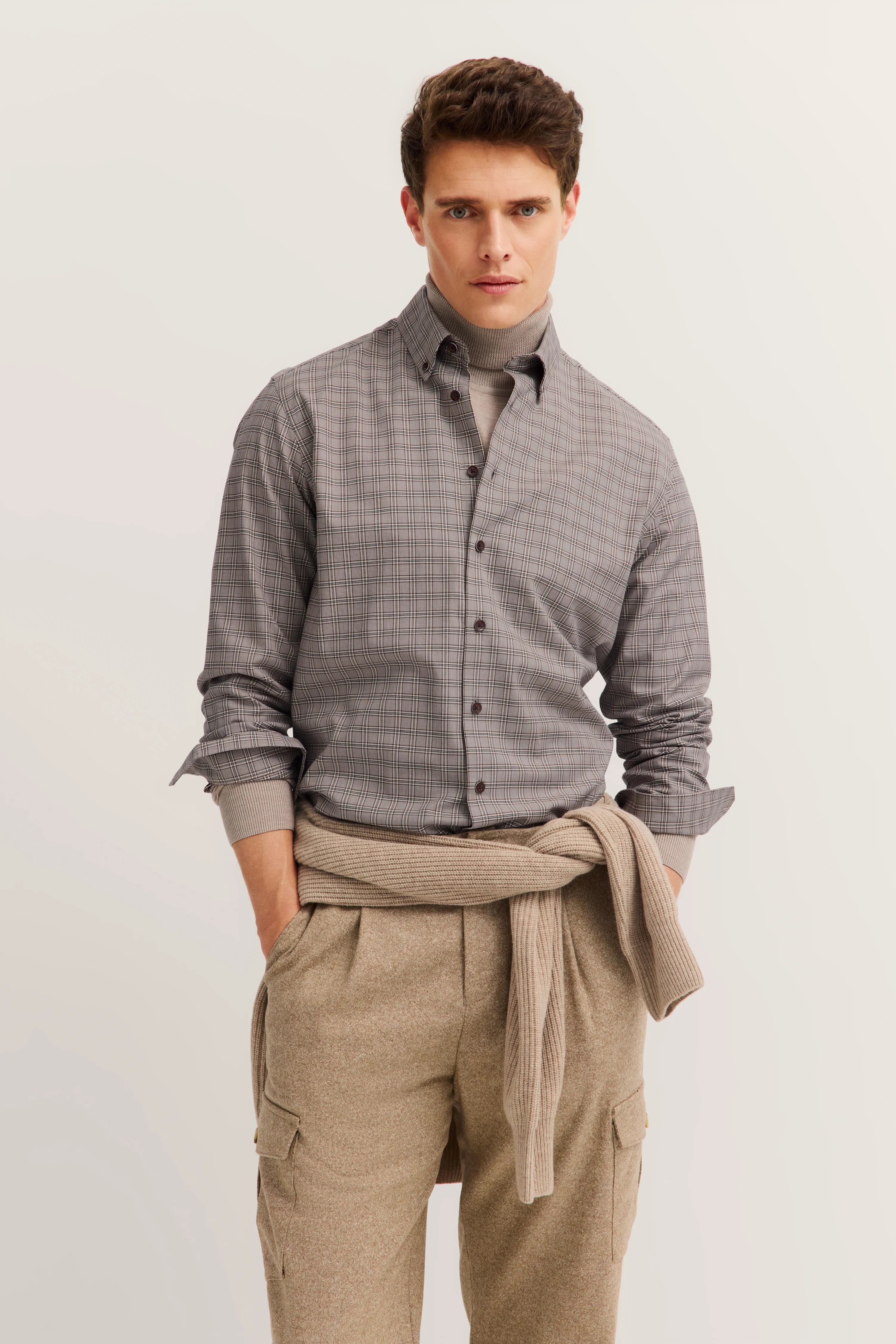 bugatti Hemd grau kariert, beige Hose, Pullover um die Taille, Model stehend, lässige Pose.