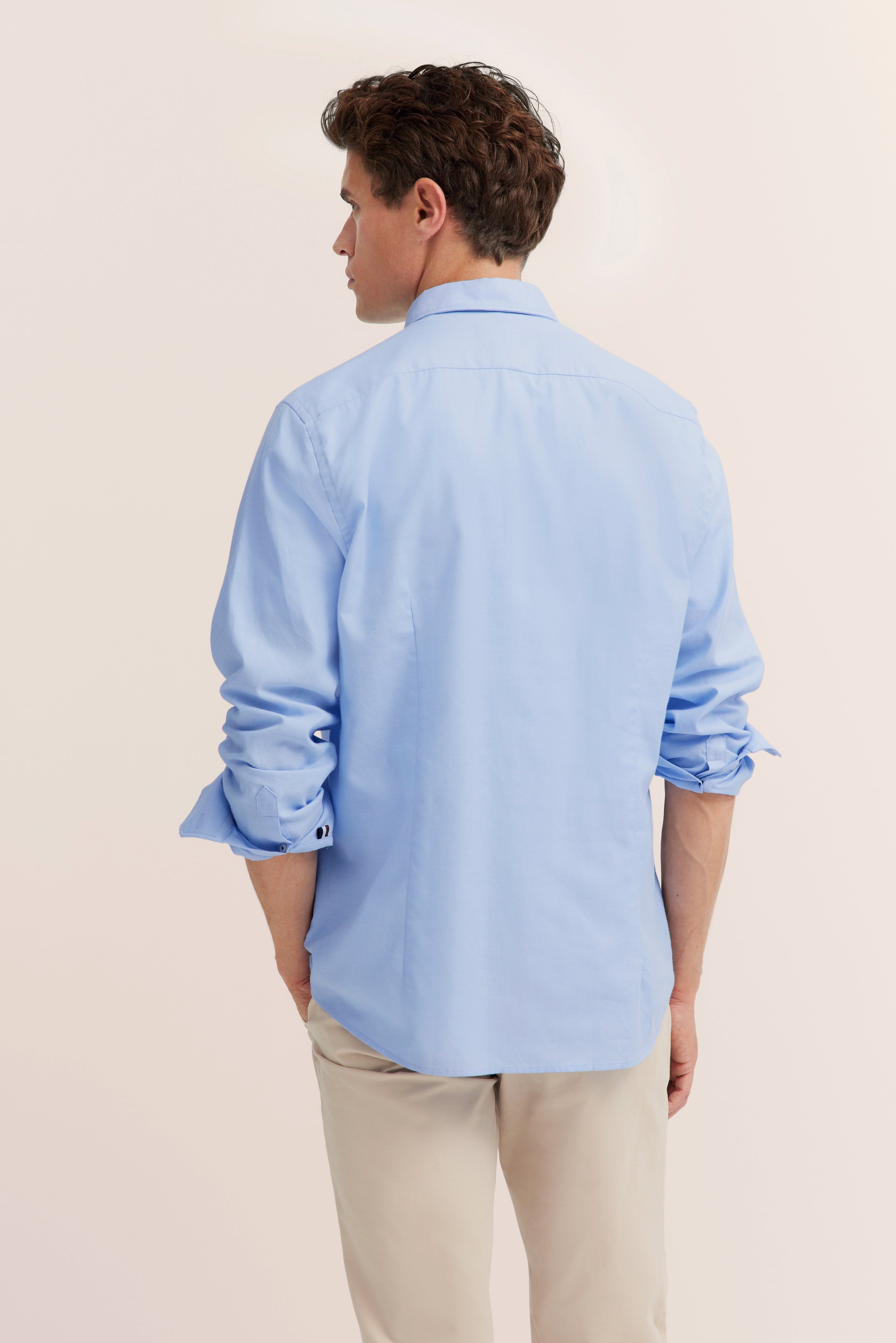 Herren-Model von hinten in hellblauem Hemd und beigen Hosen. Lässiges Posing.