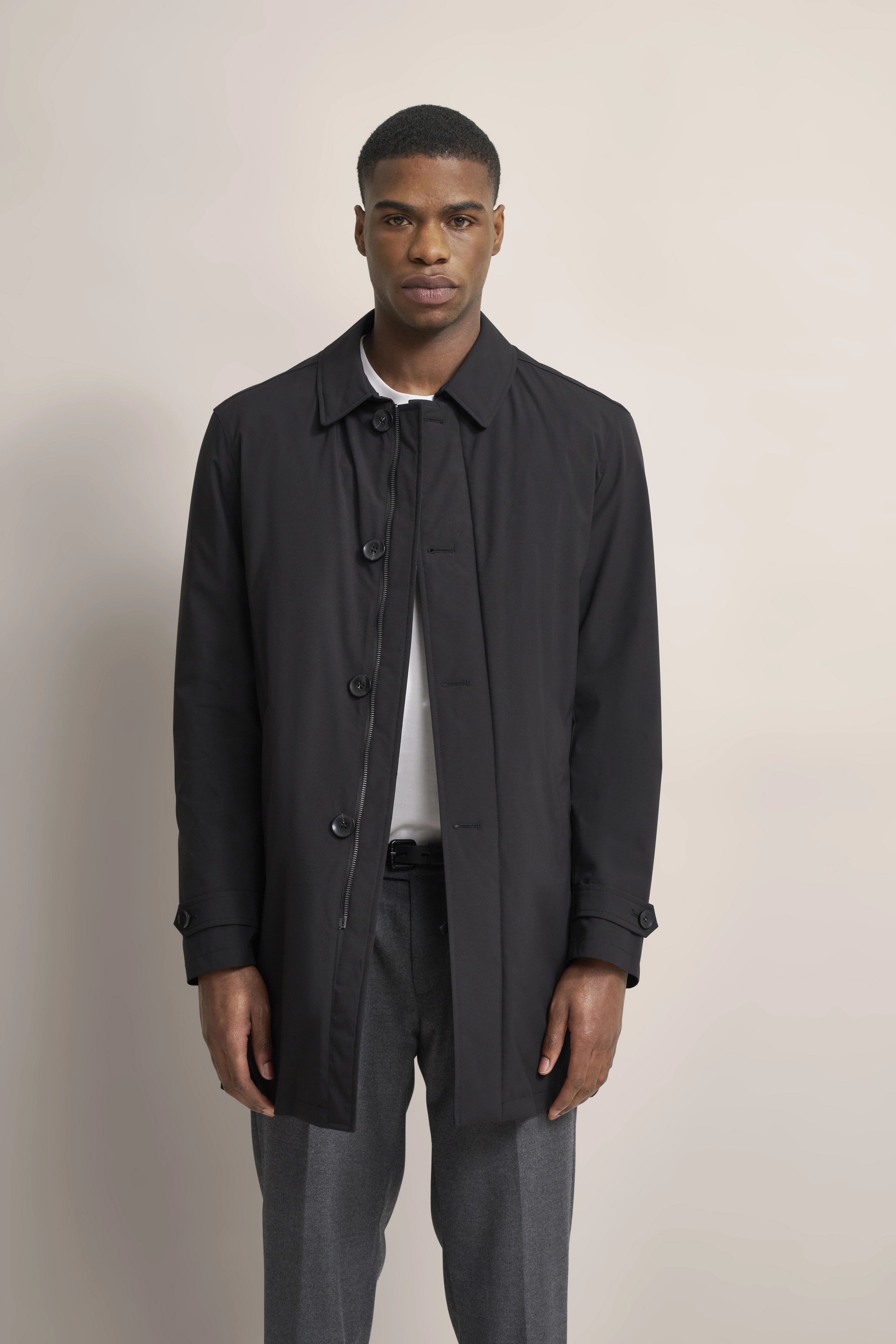 Black bugatti coat, white shirt, grey pants. Model posing frontally.
