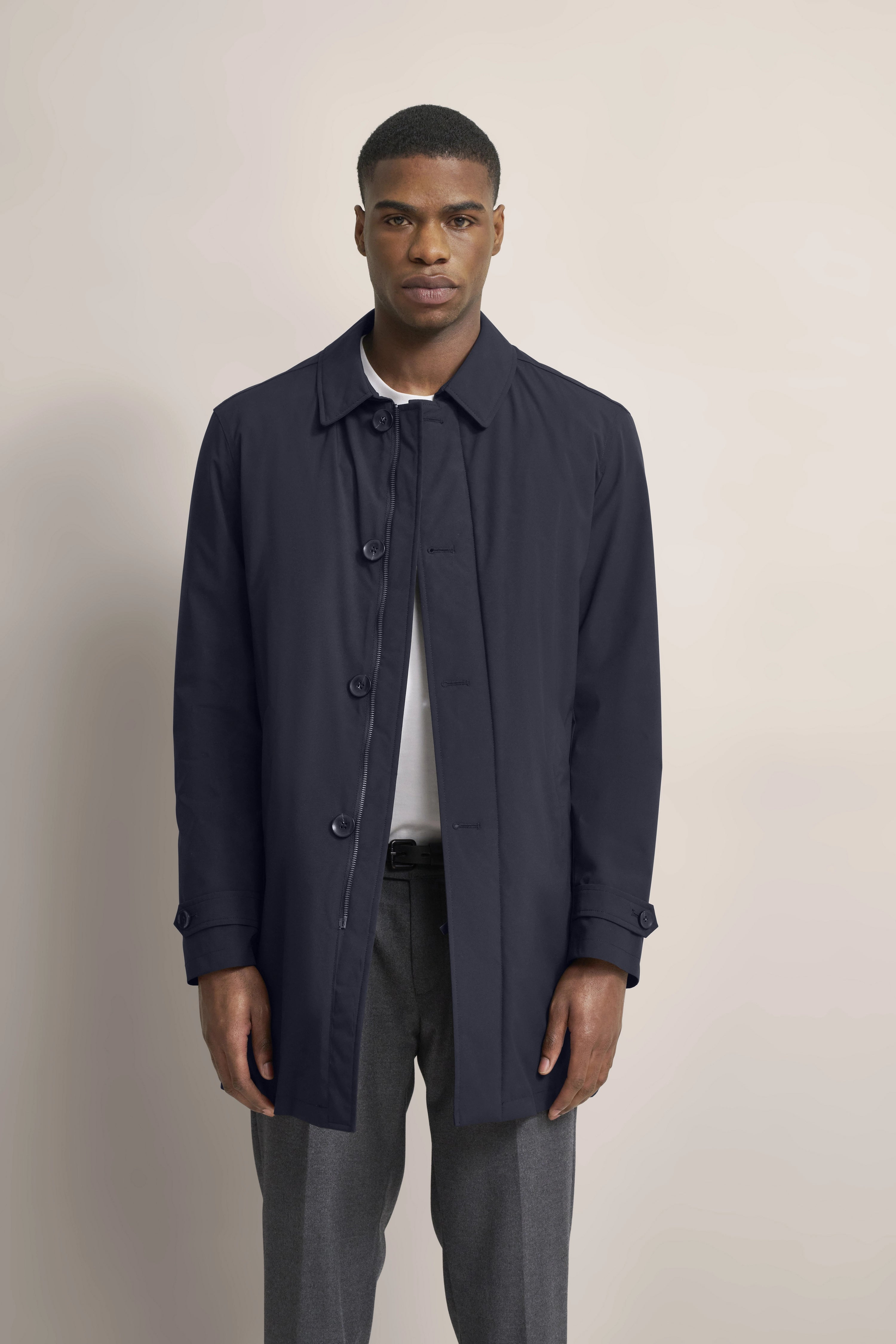 bugatti style: Dark blue coat, gray pants, white shirt. Model standing frontally.