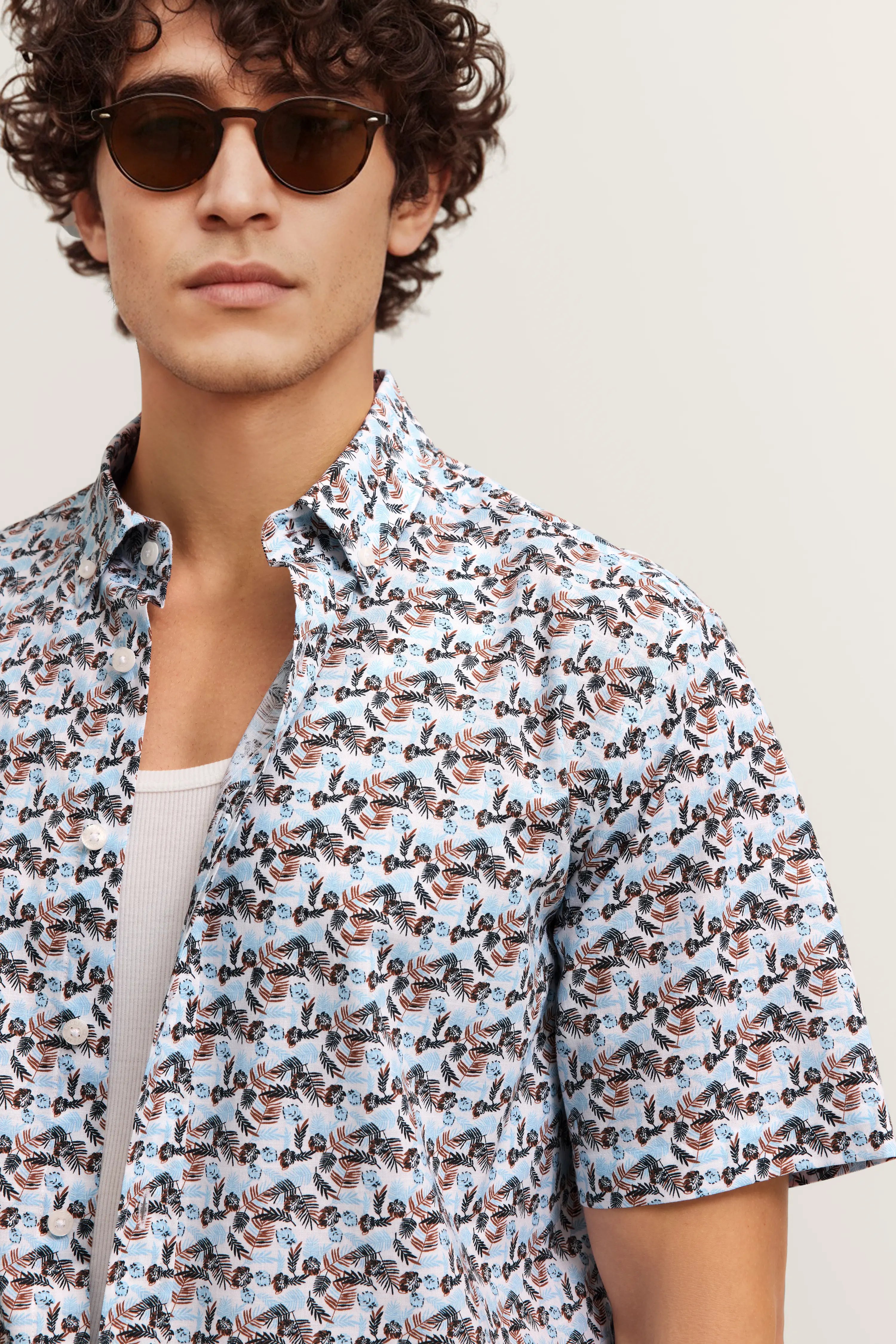 Herrenhemd mit floralem Muster in Blau und Braun, Modell trägt Sonnenbrille, legerer Look, bugatti Stil.